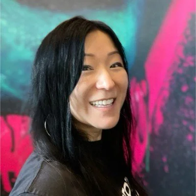 A woman with long black hair smiling at the camera, standing in front of a colorful, abstract wall.