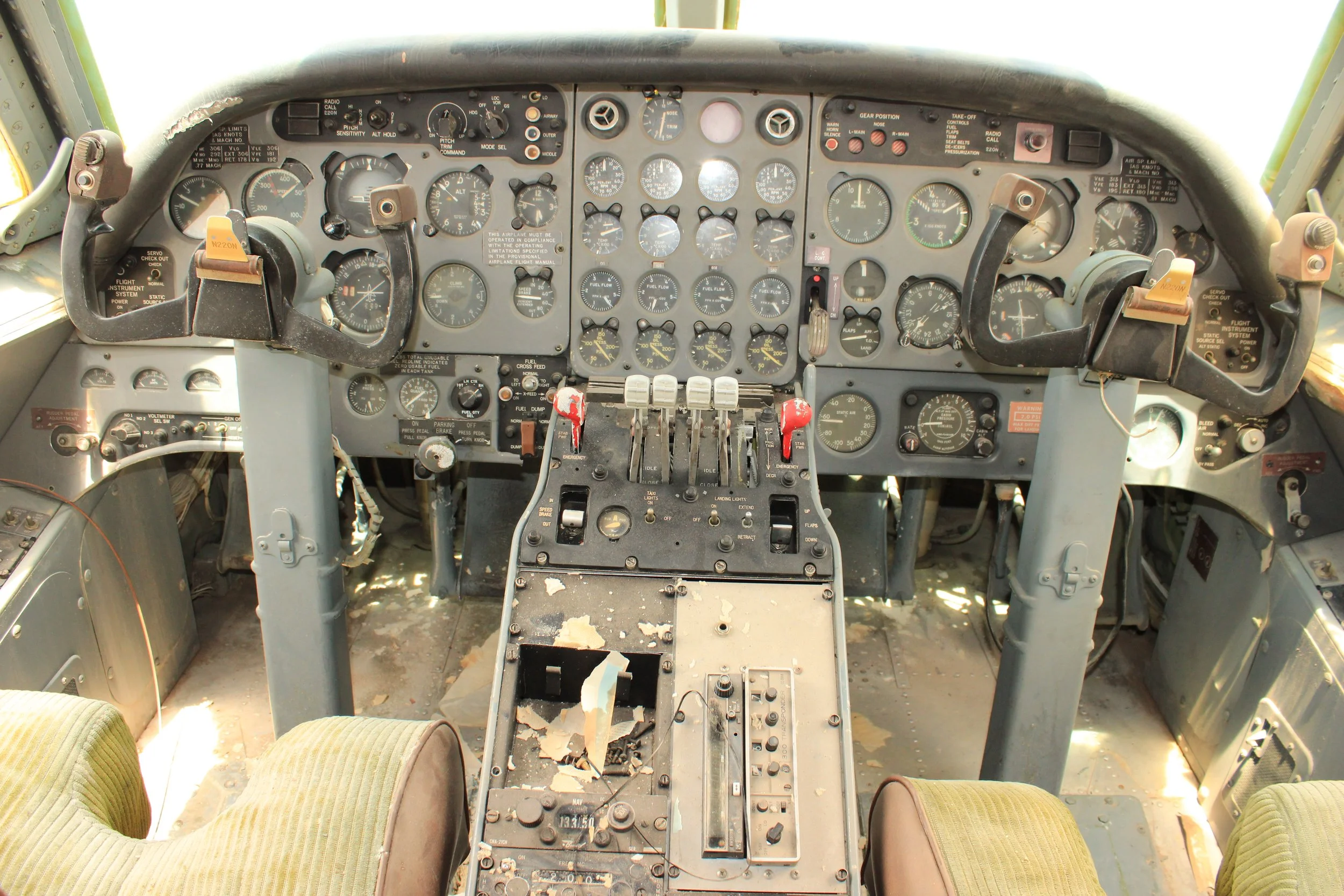 The interior cockpit of a vintage airplane with numerous gauges, switches, and controls, showing signs of wear and torn seats.