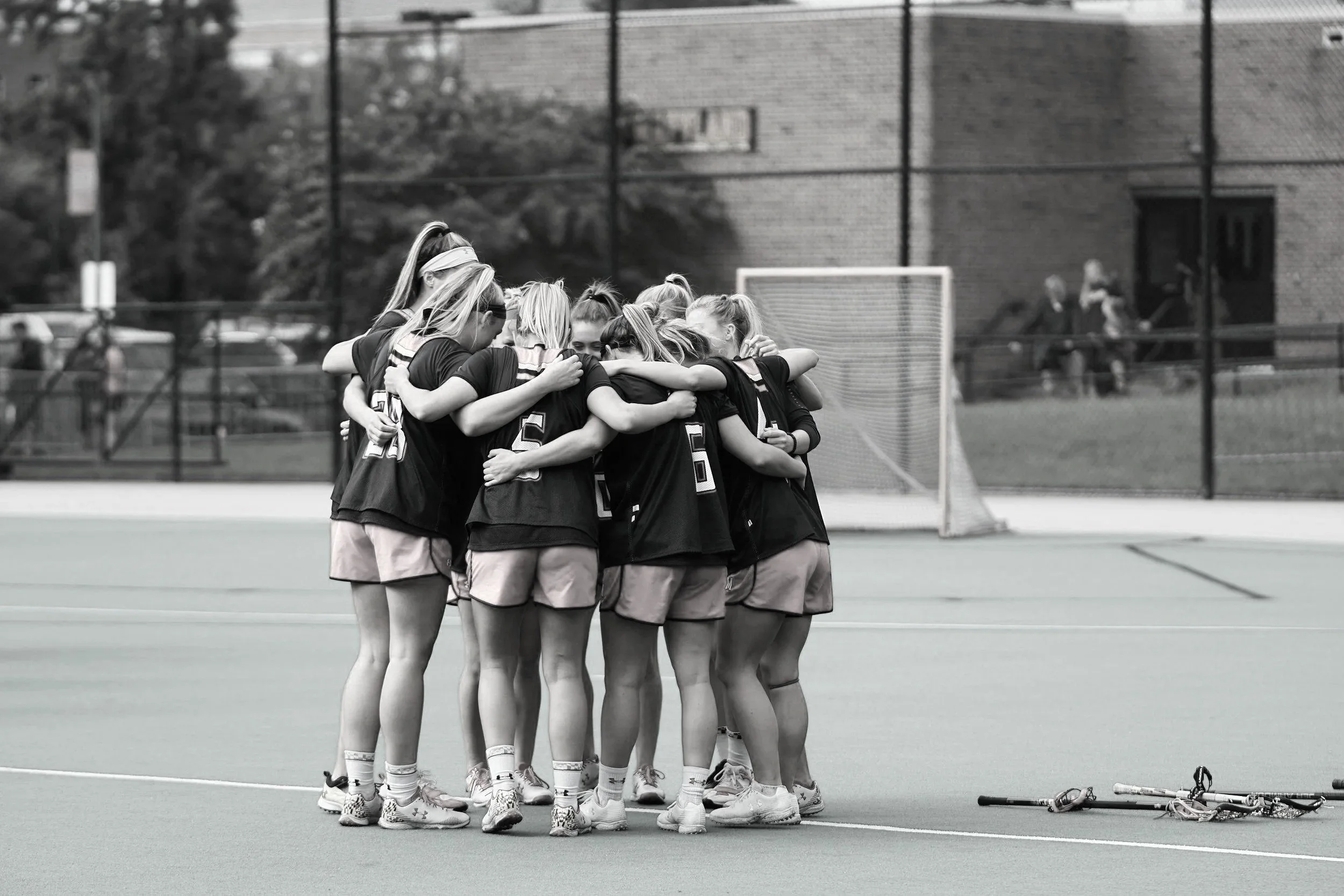 A group of female athletes in sports uniforms huddled together on a sports field.