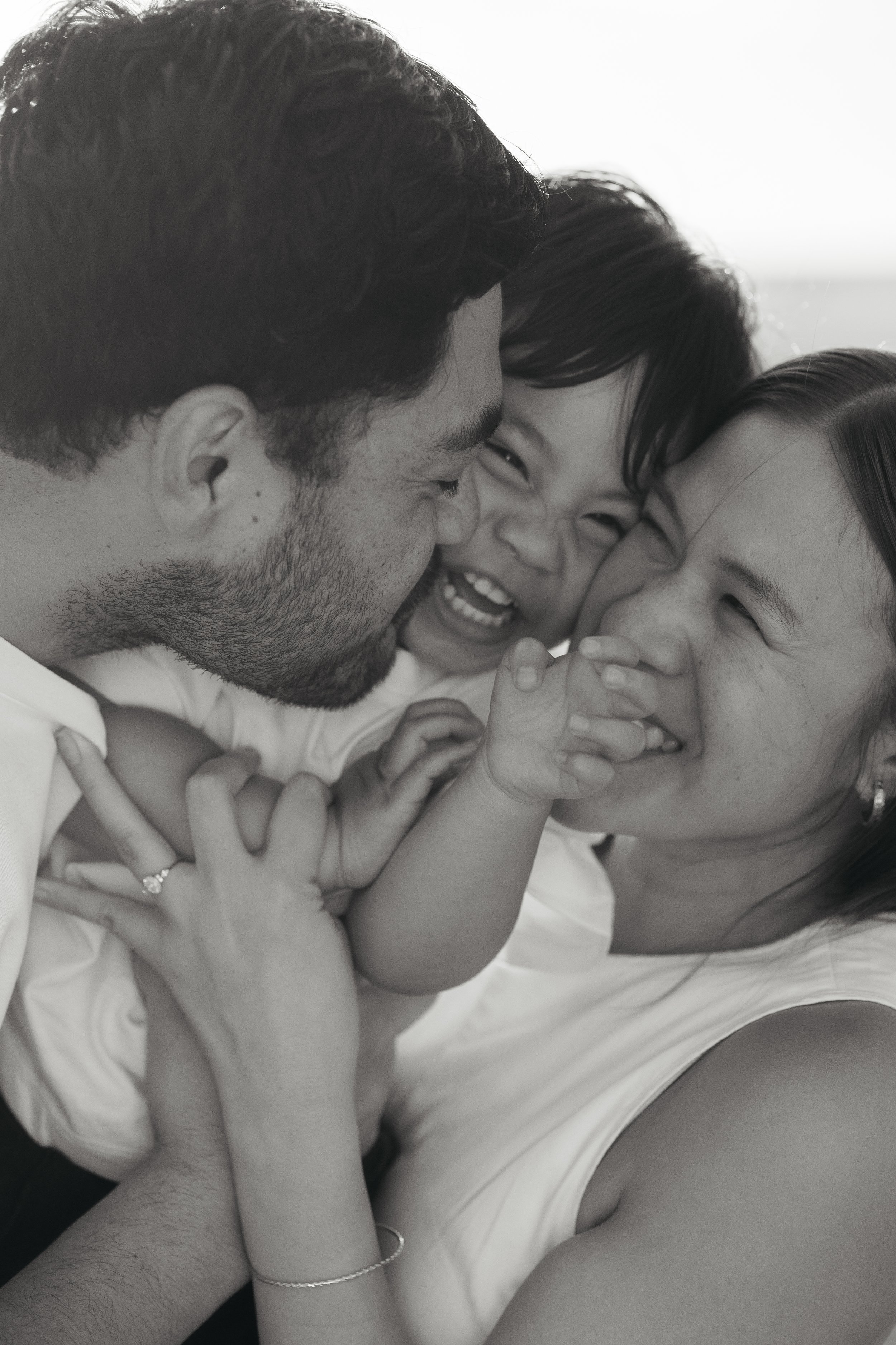 Natural family photography in Melbourne capturing parents laughing and cuddling their smiling toddler during a relaxed family session.
