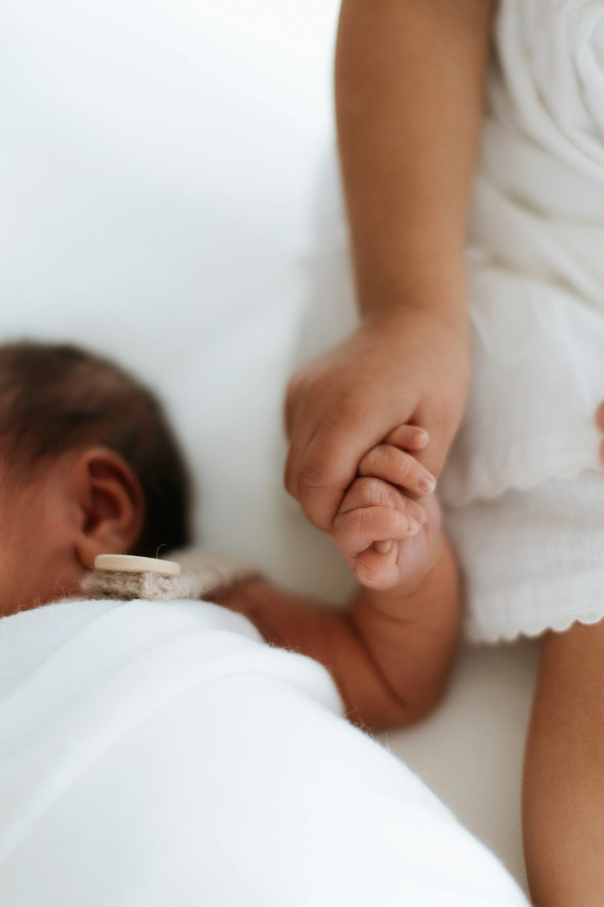 Natural newborn sibling photography in Melbourne capturing an older sibling gently holding their newborn baby’s hand.