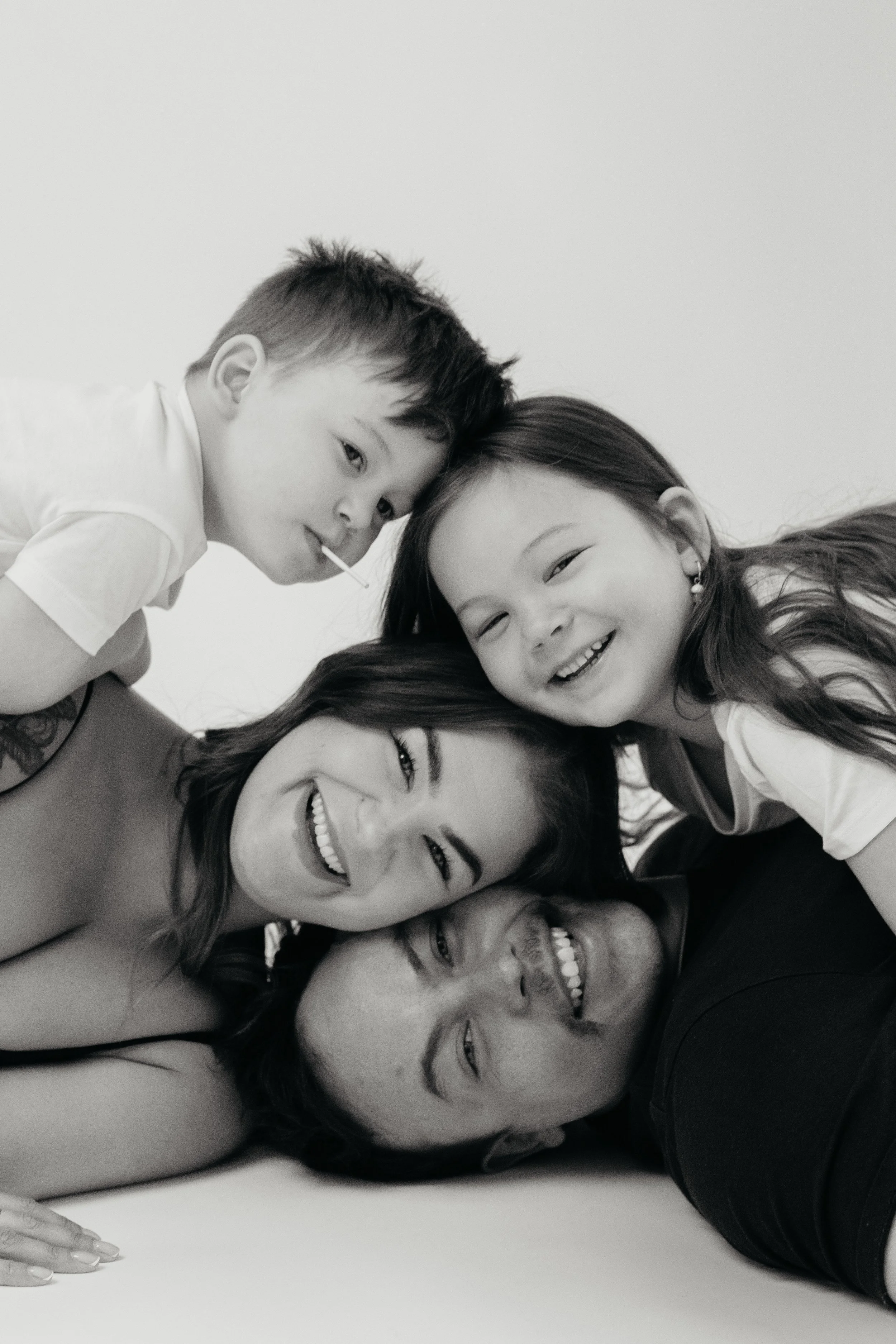 Black and white family photography in Melbourne featuring parents and two children sharing a joyful, timeless portrait.