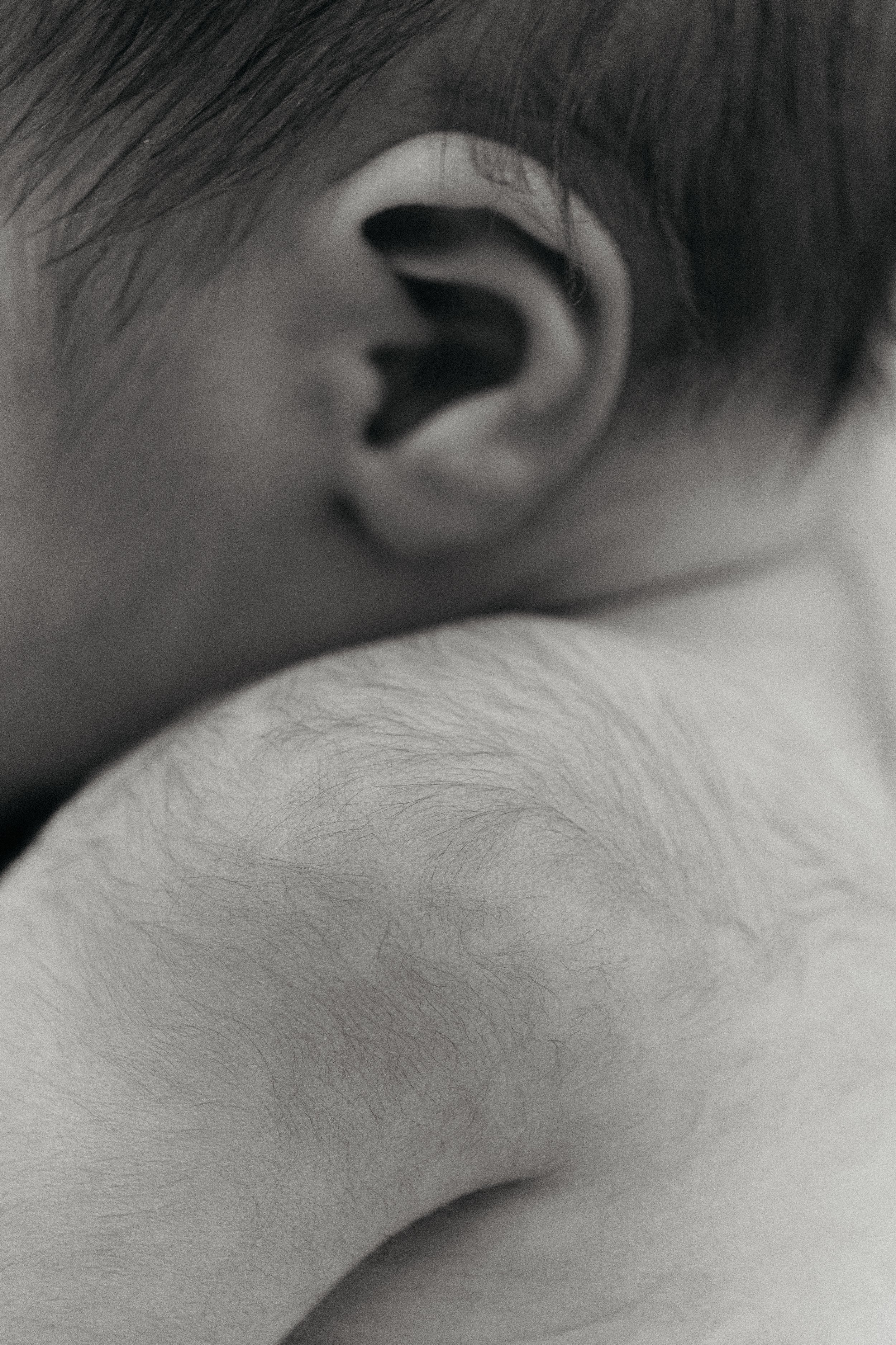 Close-up black and white photograph of a person's ear and shoulder, showing fine hair and skin details.
