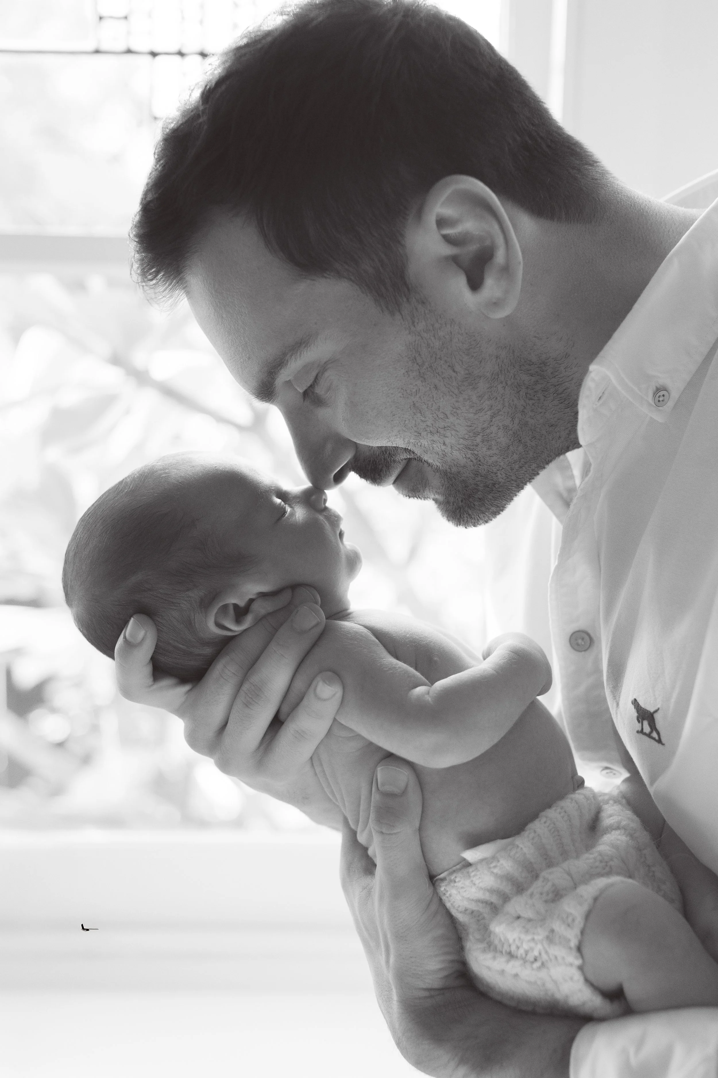Natural newborn photography in Melbourne of a father gently holding and touching noses with his newborn baby in a timeless black and white portrait.