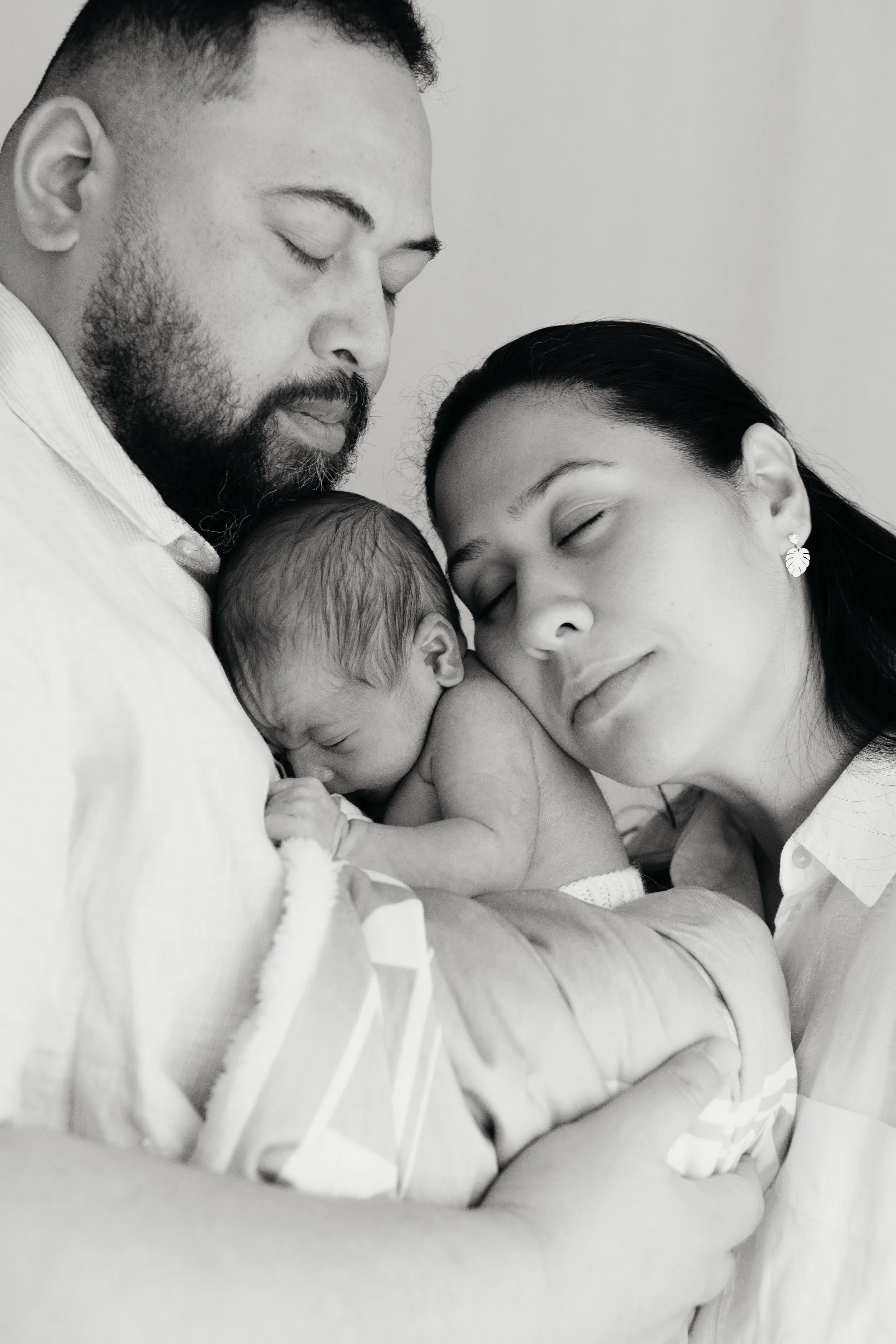 Black and white photograph of a family with two adults and a baby, all peacefully sleeping in close embrace.