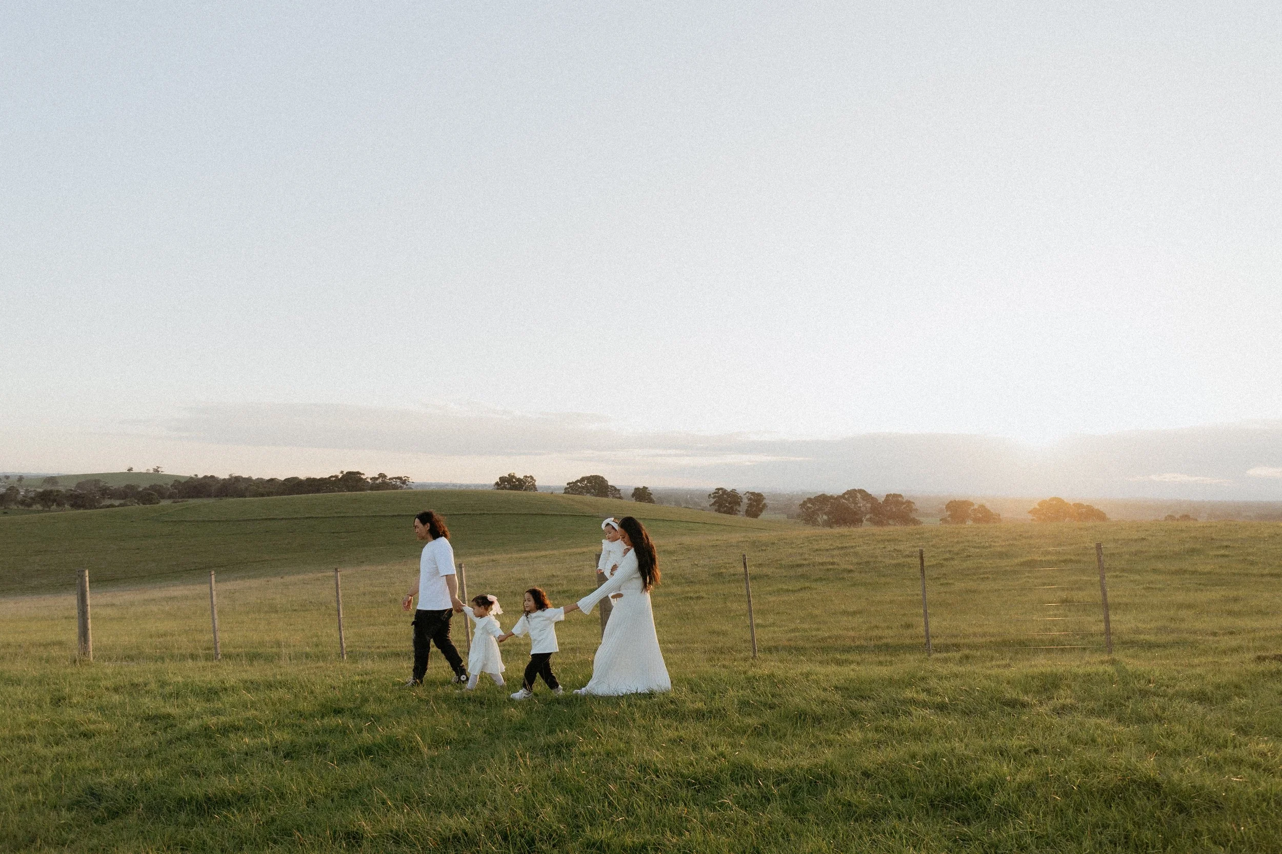 Family photography in Melbourne capturing parents and their young children walking together through an open field at golden hour.