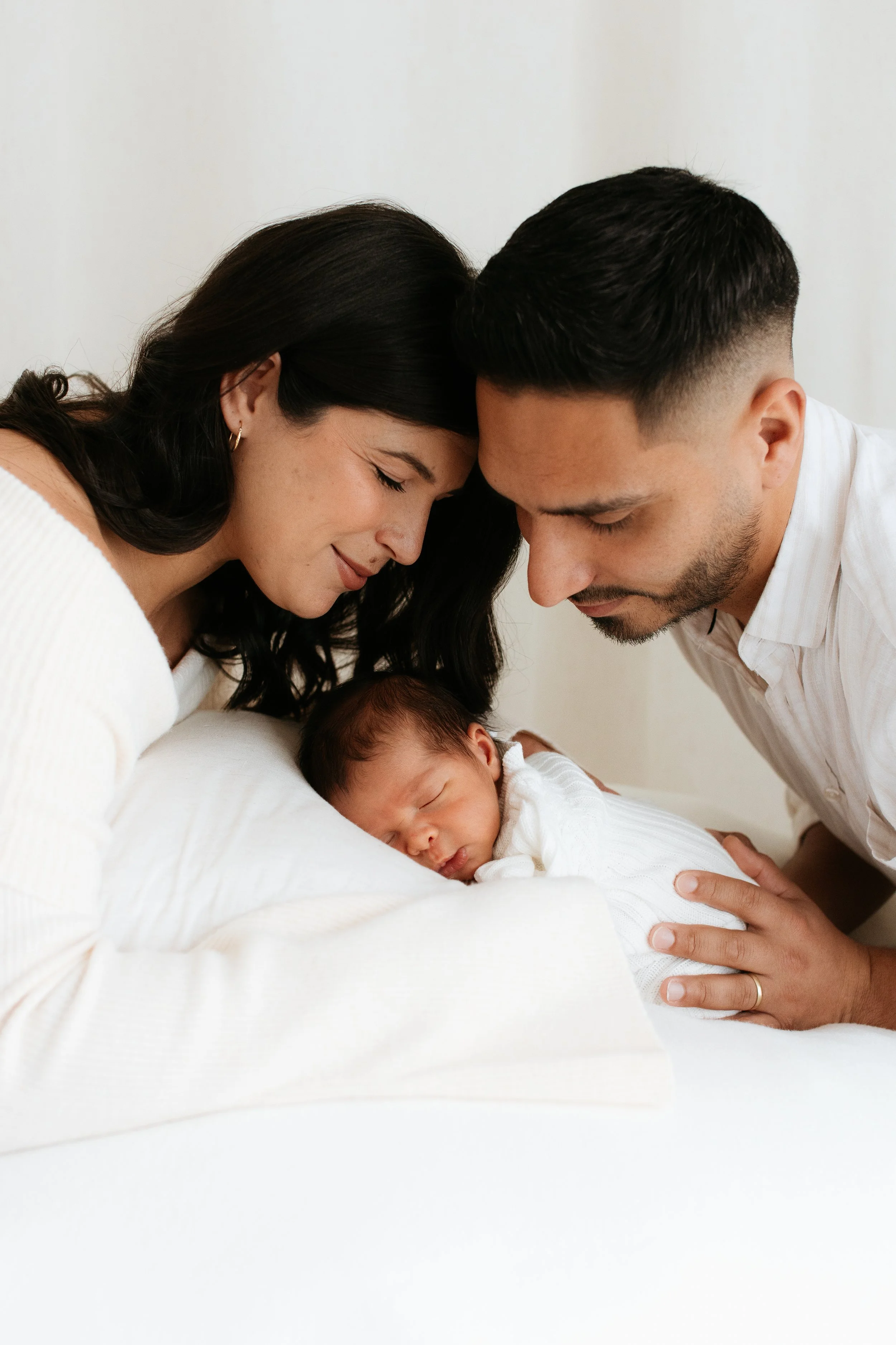 Timeless newborn family portrait by a Melbourne newborn photographer, featuring parents embracing their sleeping baby in soft natural light.