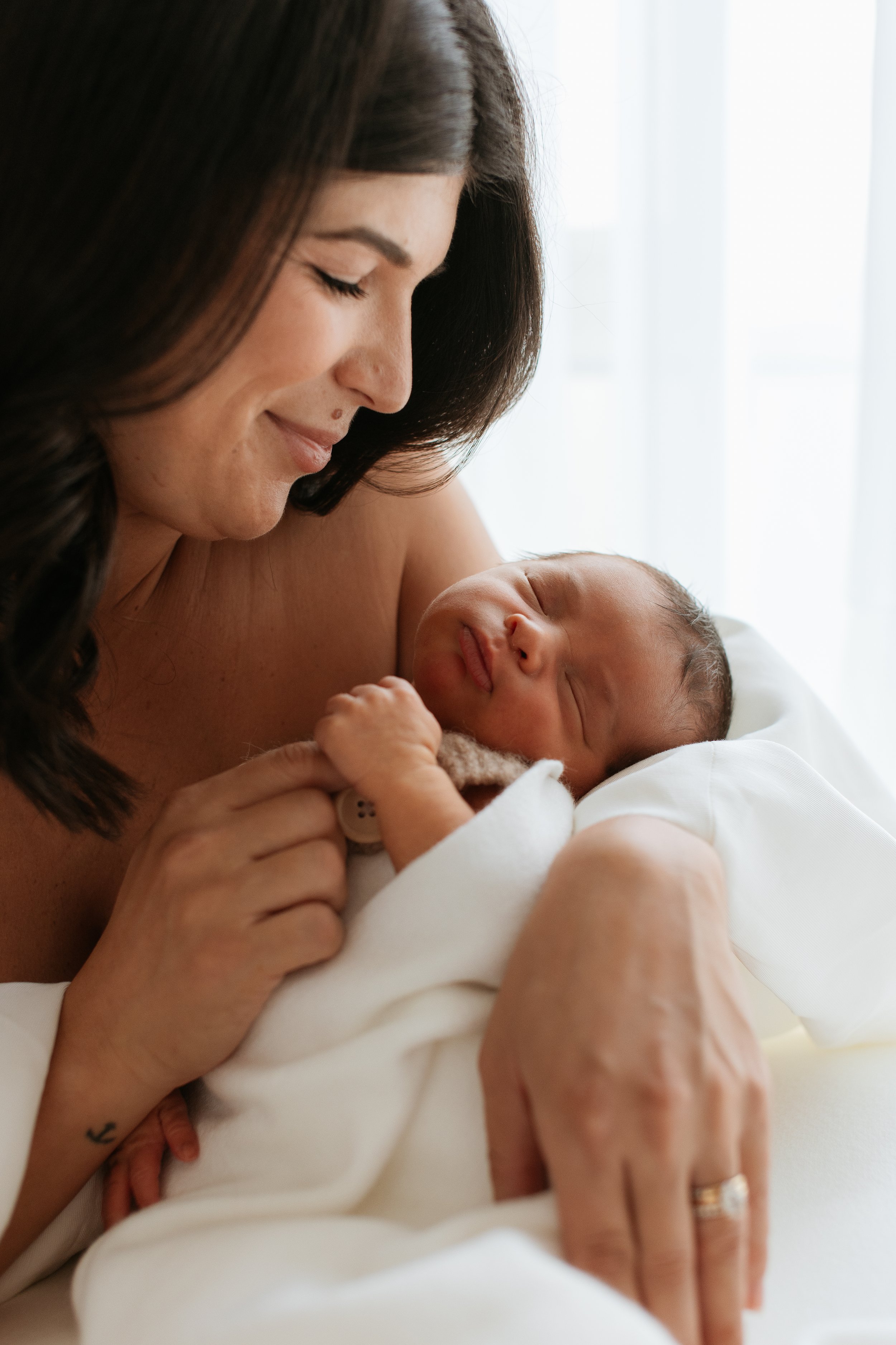 A woman holding a newborn baby close to her face, both with eyes closed, in a bright setting.
