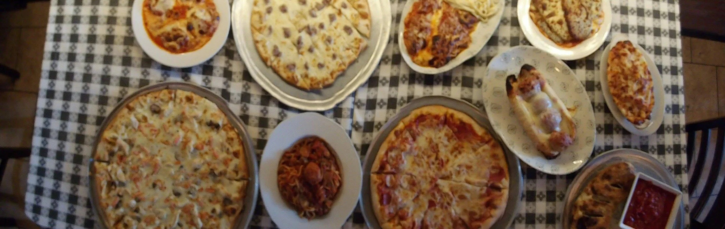 Various pizzas on plates and a bowl of chili on a checkered tablecloth.