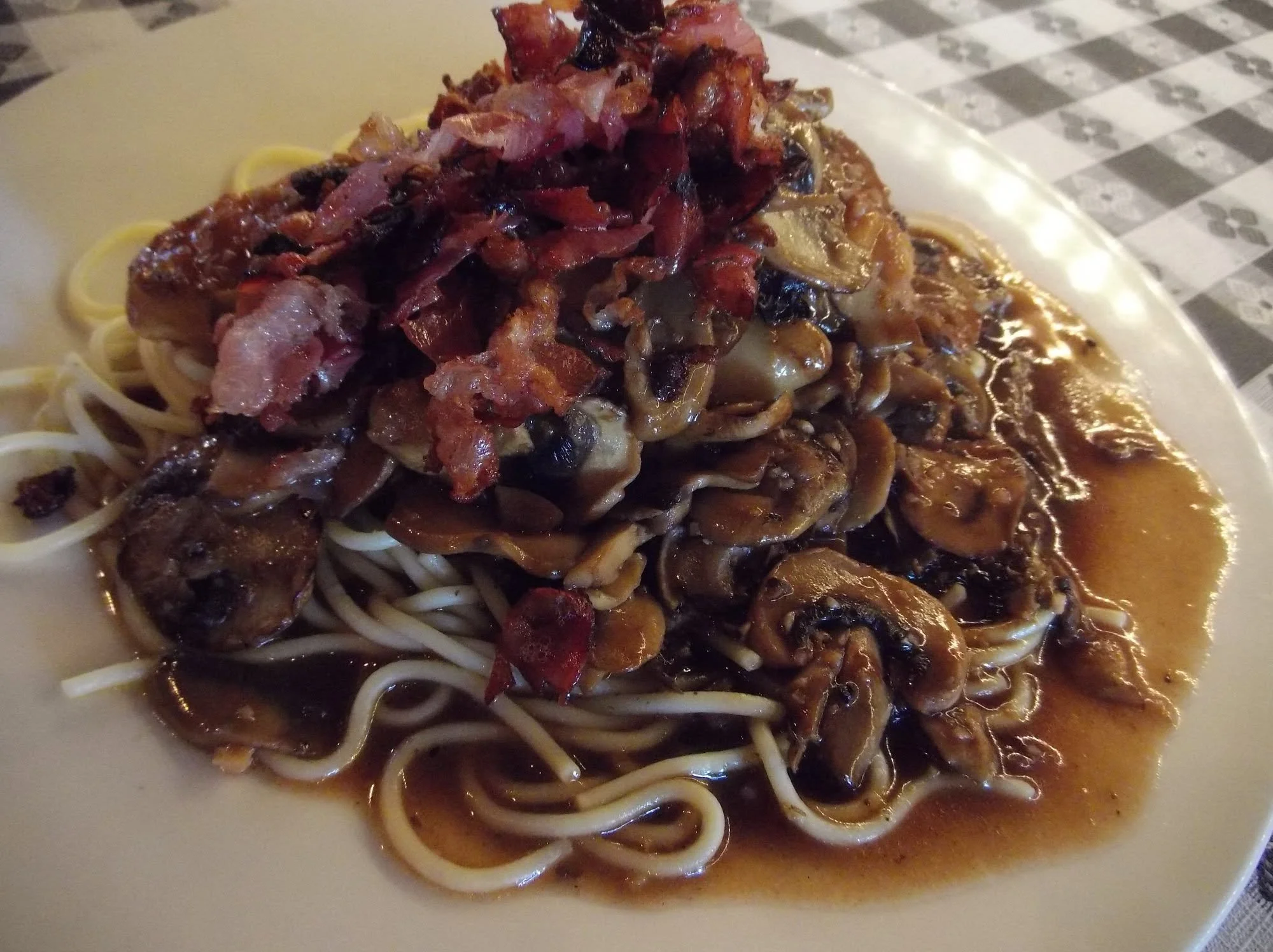 Spaghetti topped with a rich meat and vegetable sauce, garnished with crispy bacon bits, served on a white plate.
