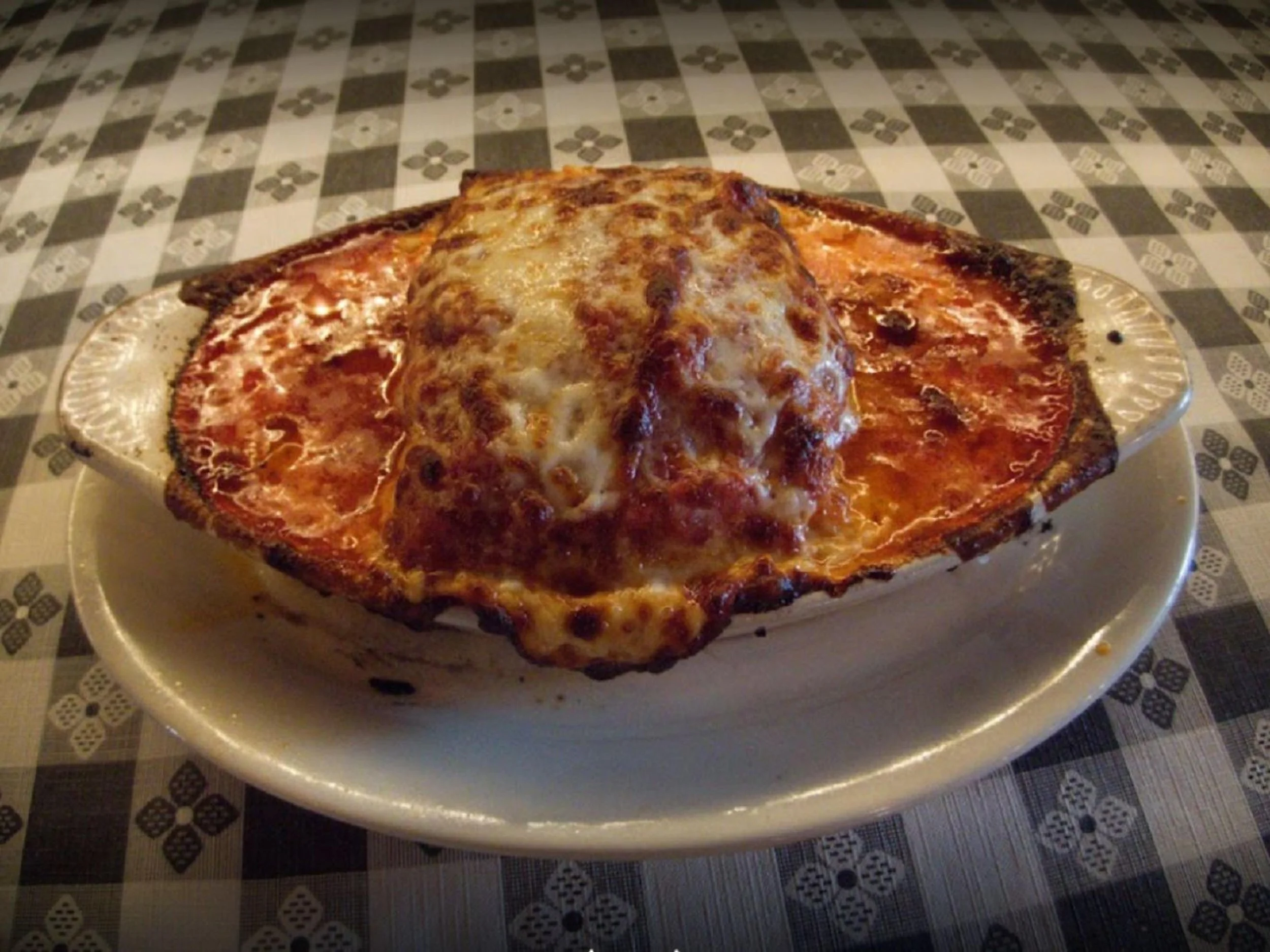 Baked lasagna with melted cheese on top served on a decorative white plate.