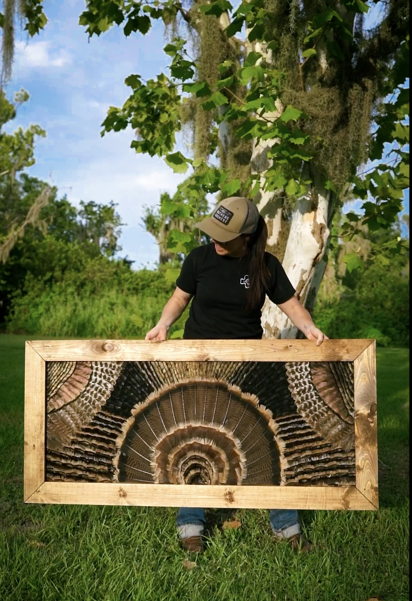 Person holding a large framed wood cross-section with intricate rings in front of a tree in a grassy outdoor setting.