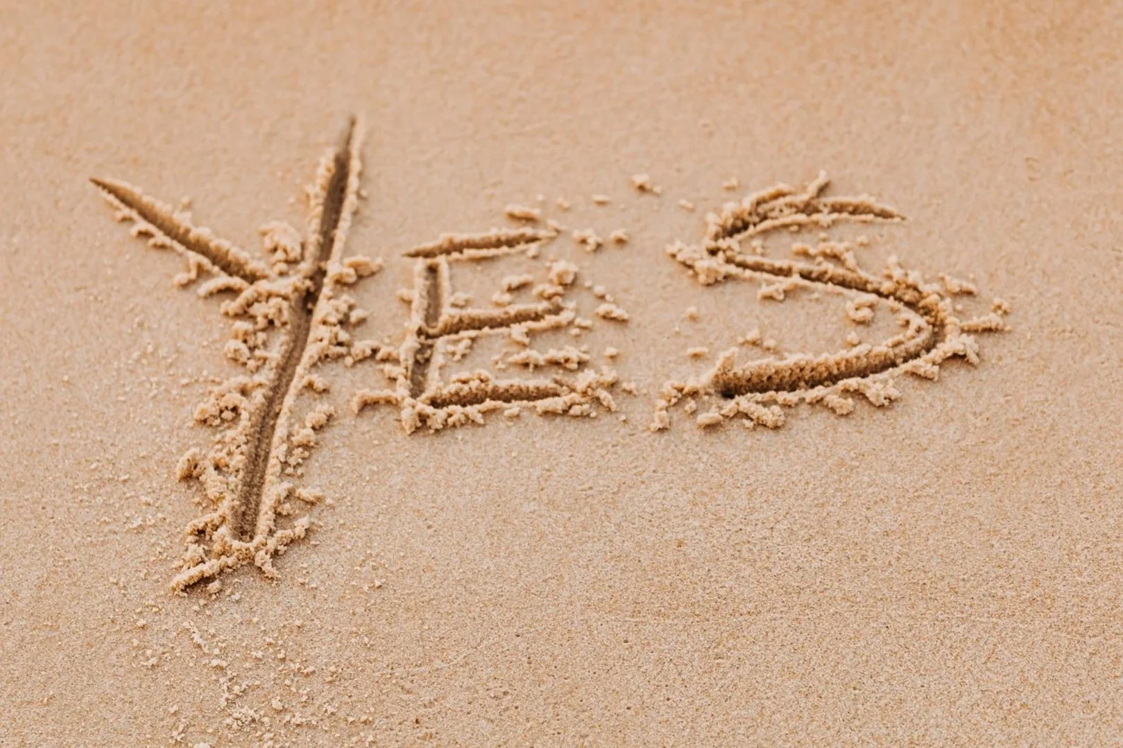 The word 'Yes' written in sand with an arrow pointing to the left of the 'Y'.