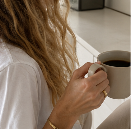 Person with long, wavy blonde hair holding a gray mug filled with coffee