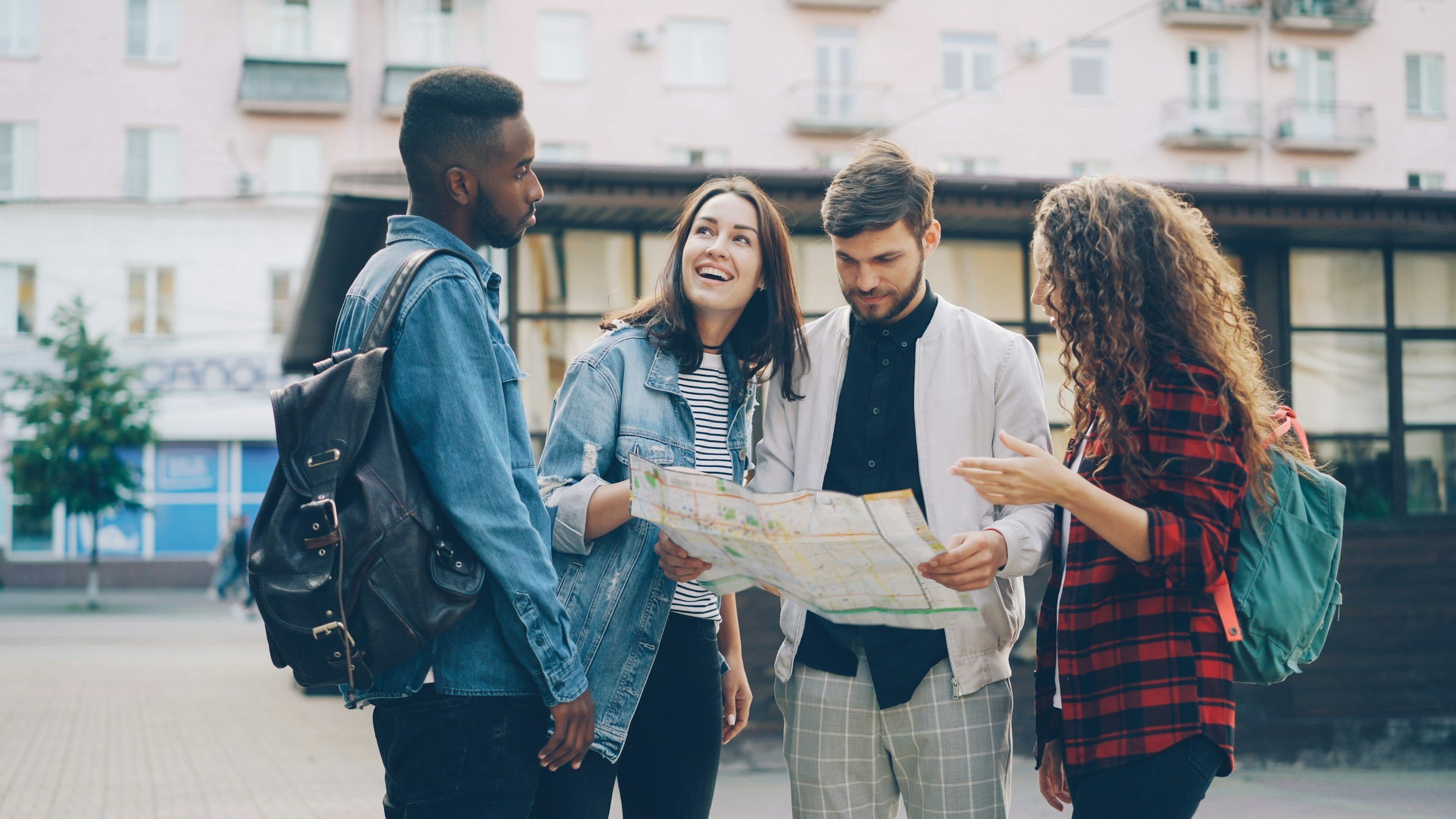 Four young adults gathered outdoors looking at a map, engaging in conversation, with residential buildings in the background.