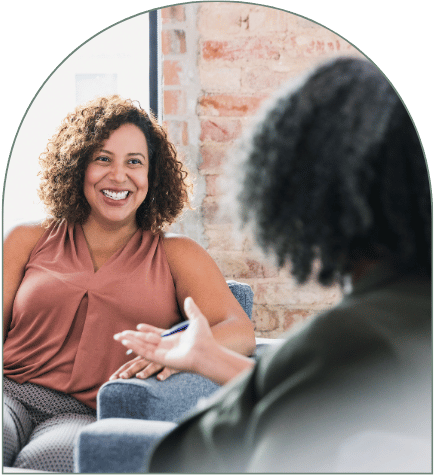 Two women having a conversation in an office setting, smiling and gesturing.