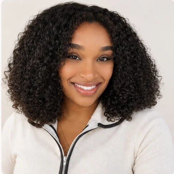 A woman with curly hair smiling, wearing a light-colored zip-up jacket.