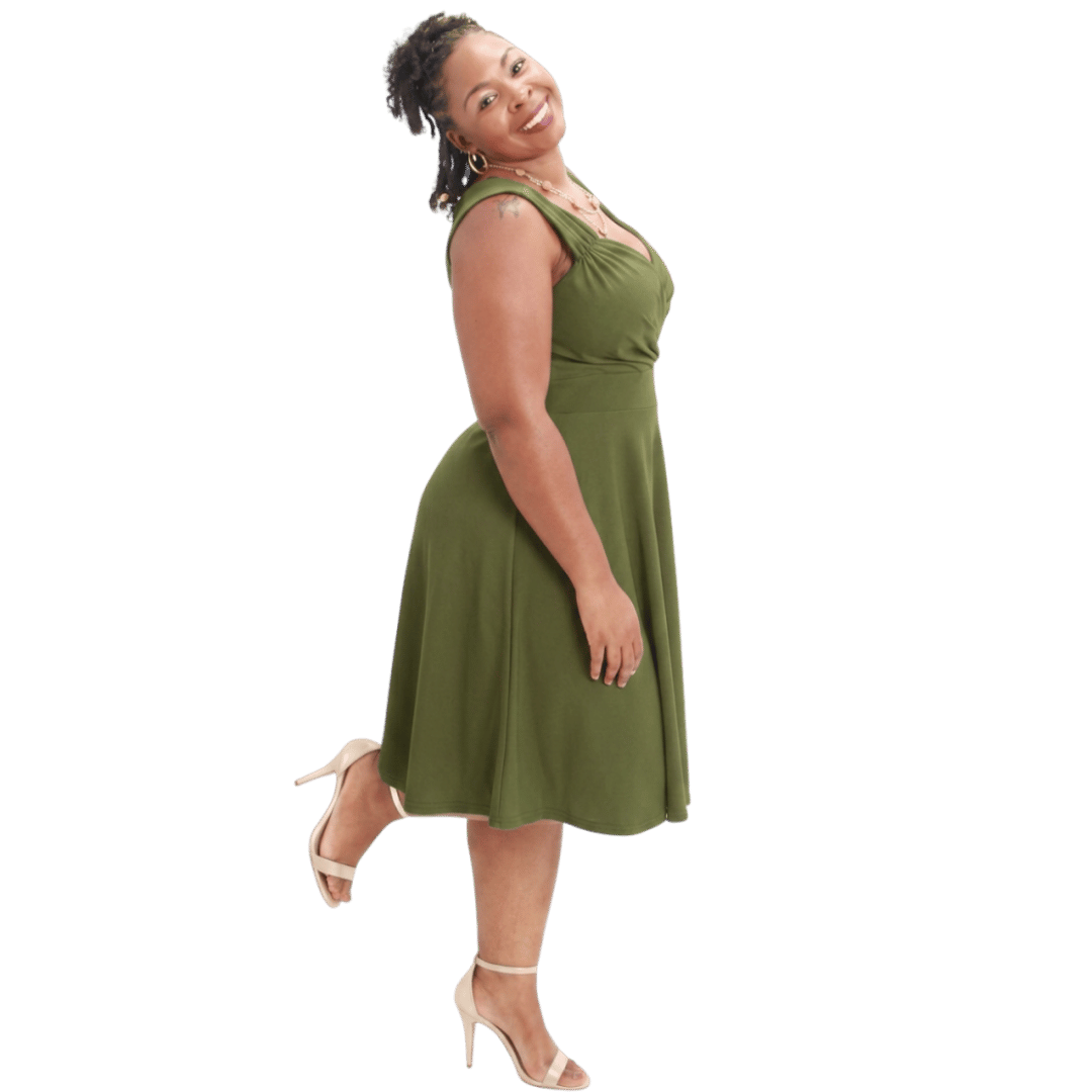 A woman with dark brown hair styled in dreadlocks wearing a green sleeveless midi dress and beige high heels, smiling and posing against a transparent background.