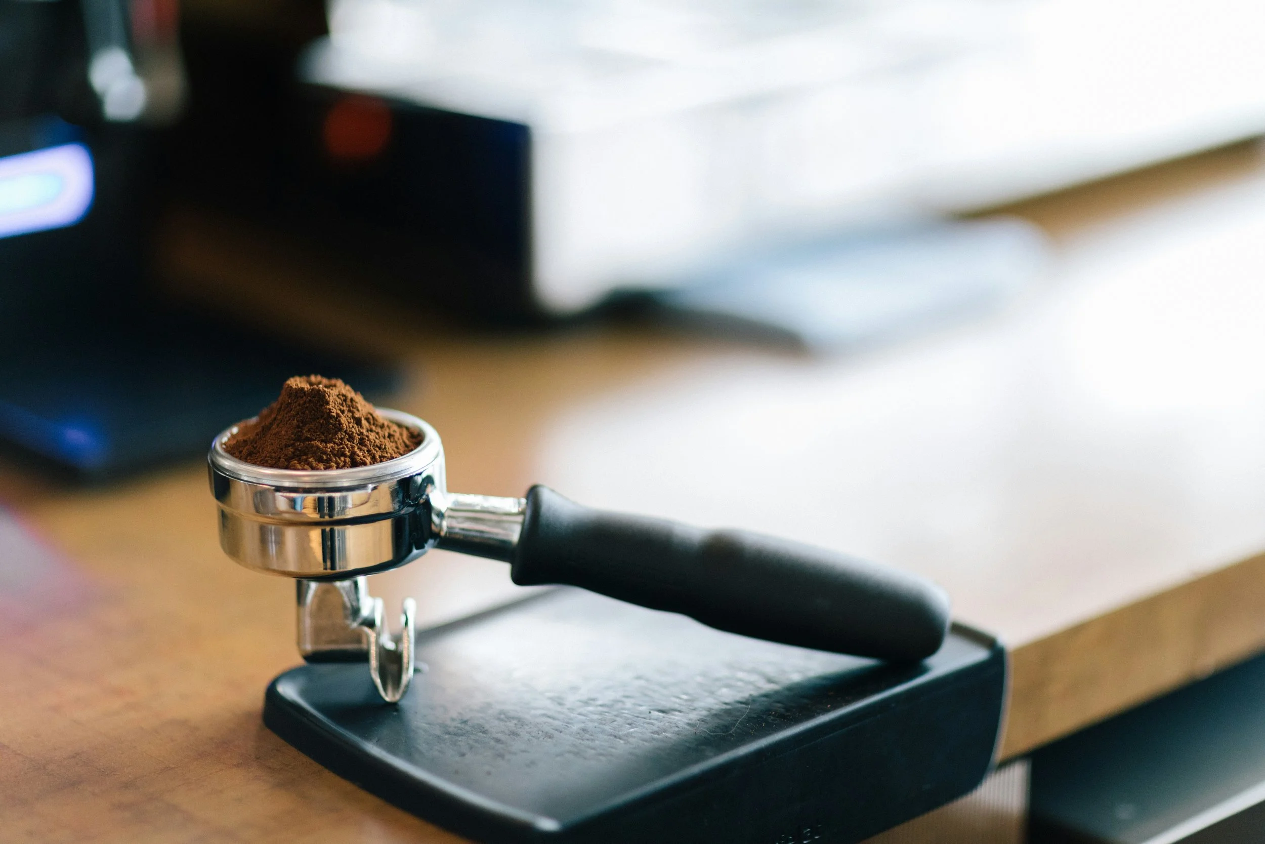 Close-up of a stainless steel portafilter filled with ground coffee on a coffee machine, with a blurred background.