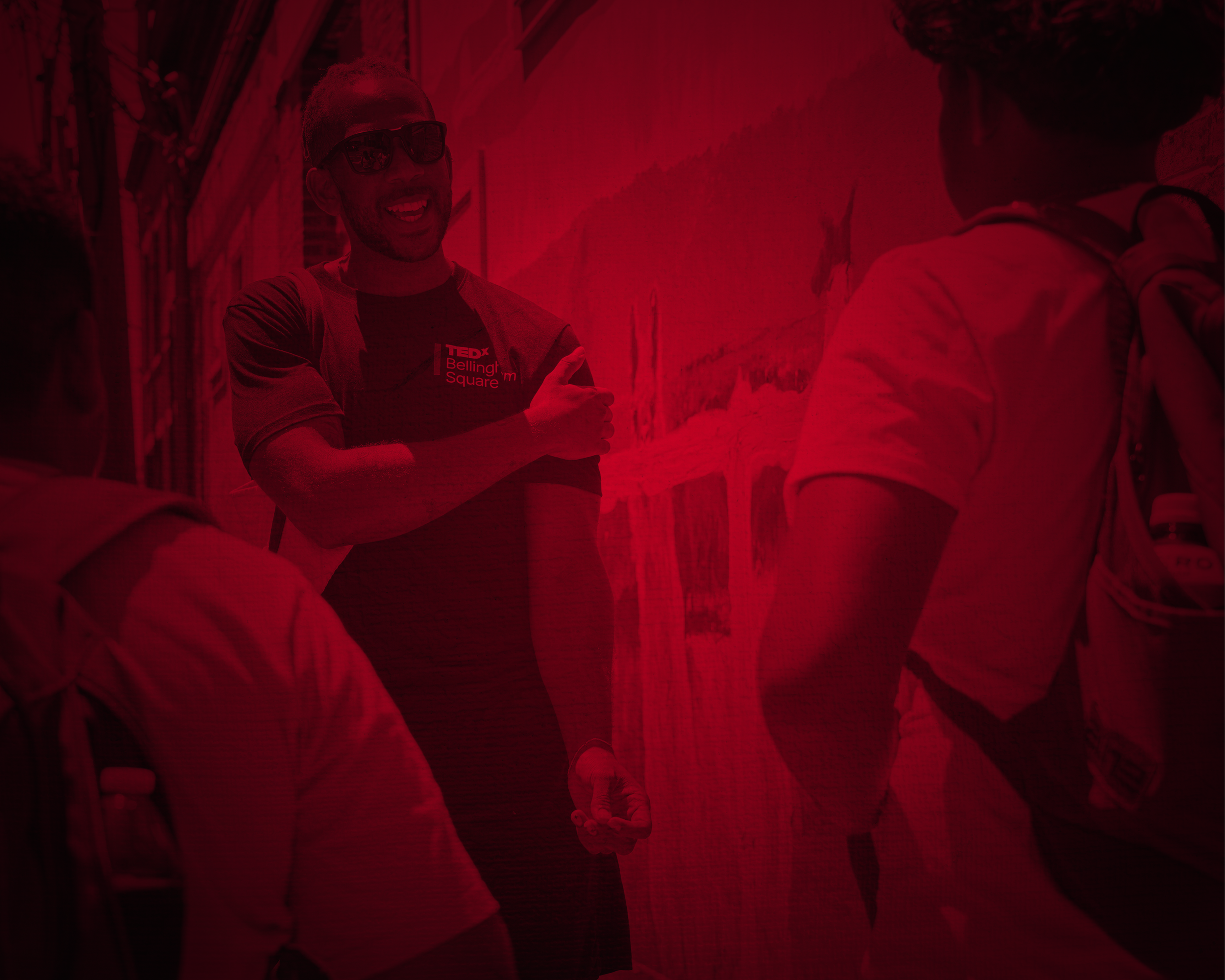 Three people, engaging in conversation outdoors, with one person smiling wearing sunglasses and a T-shirt with a TEDx Bellingham Square logo.