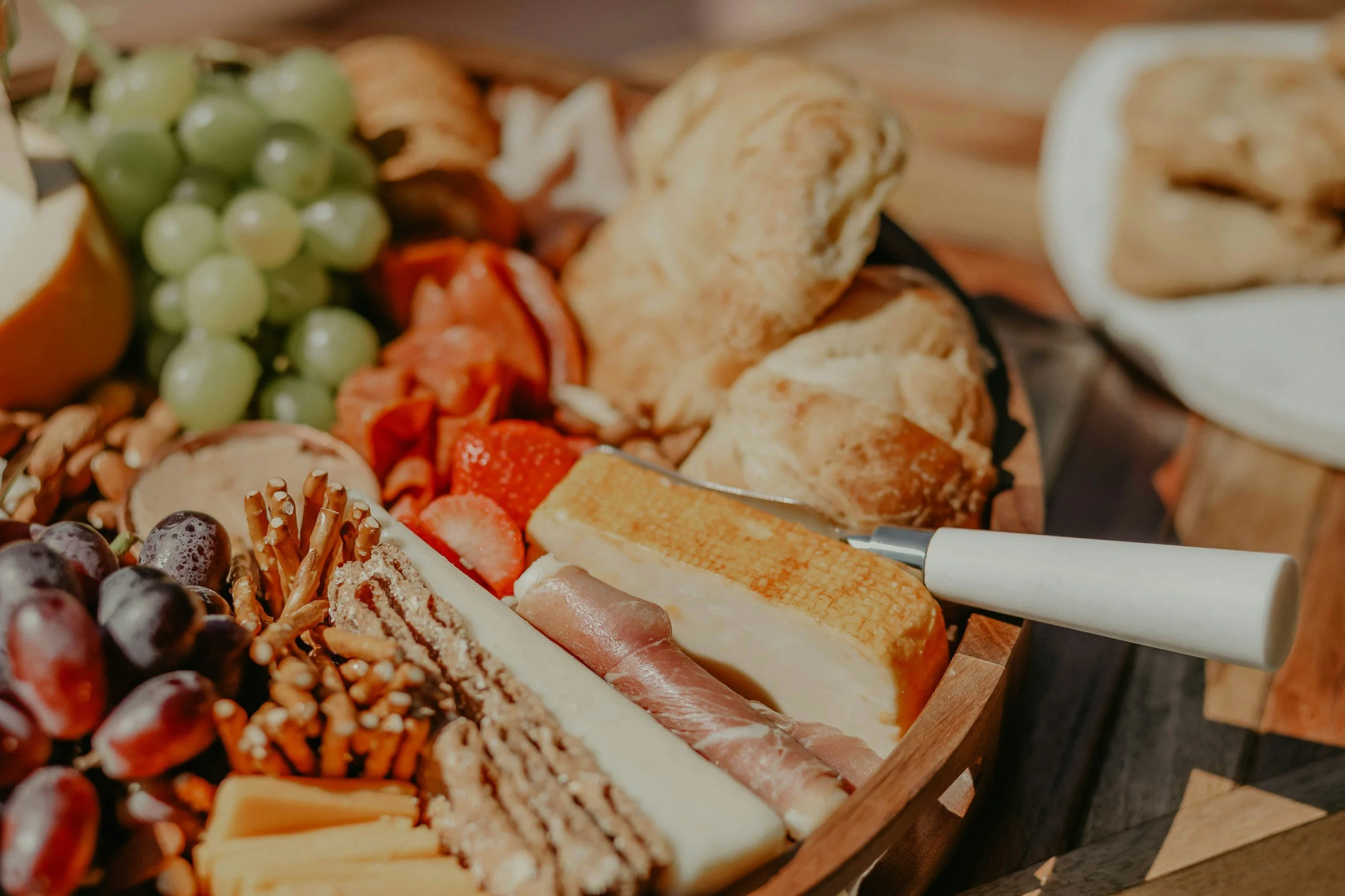 A wooden charcuterie board with a variety of cheeses, grapes, strawberries, and nuts, along with a white cheese knife.