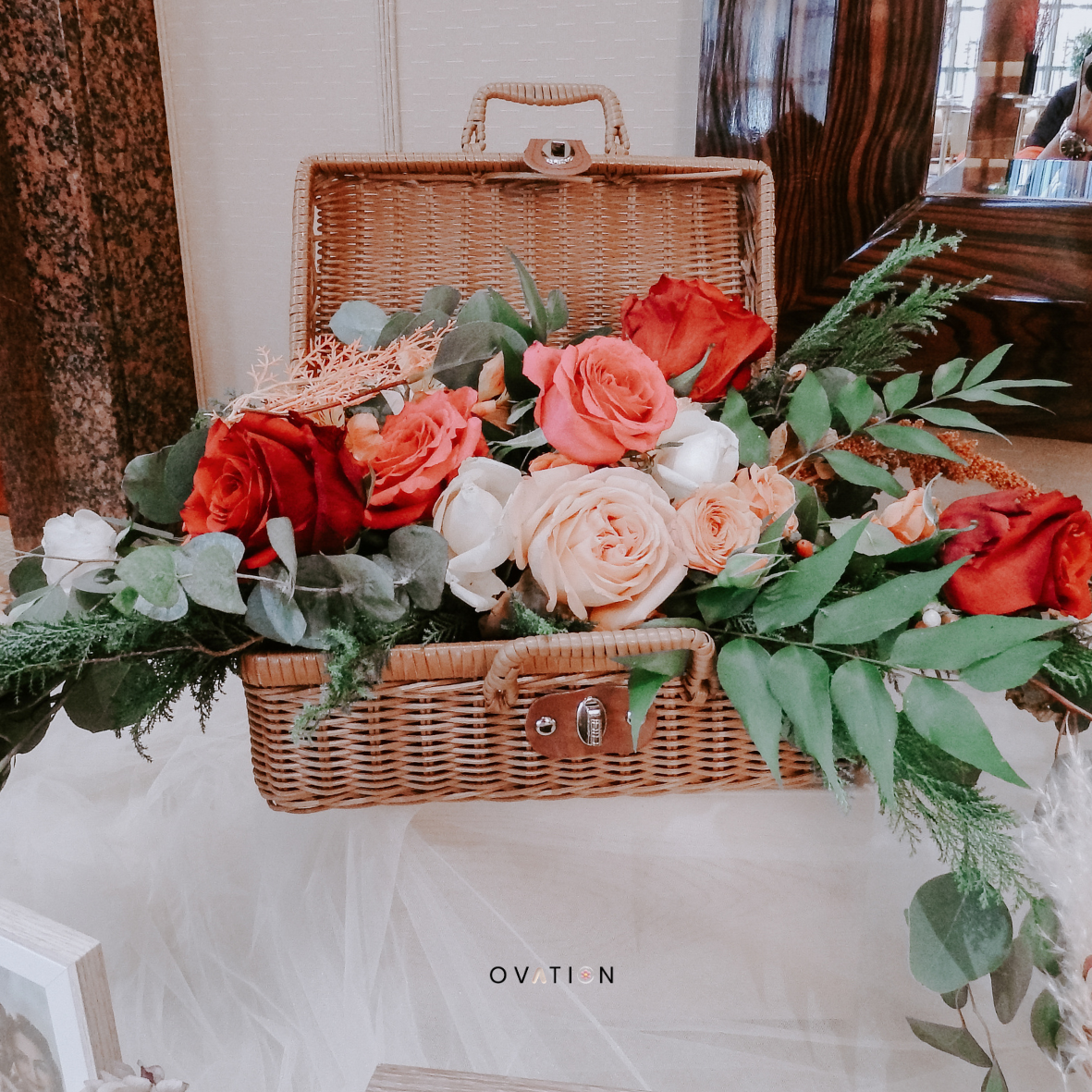 A floral arrangement with red, orange, and white roses in a wicker basket.