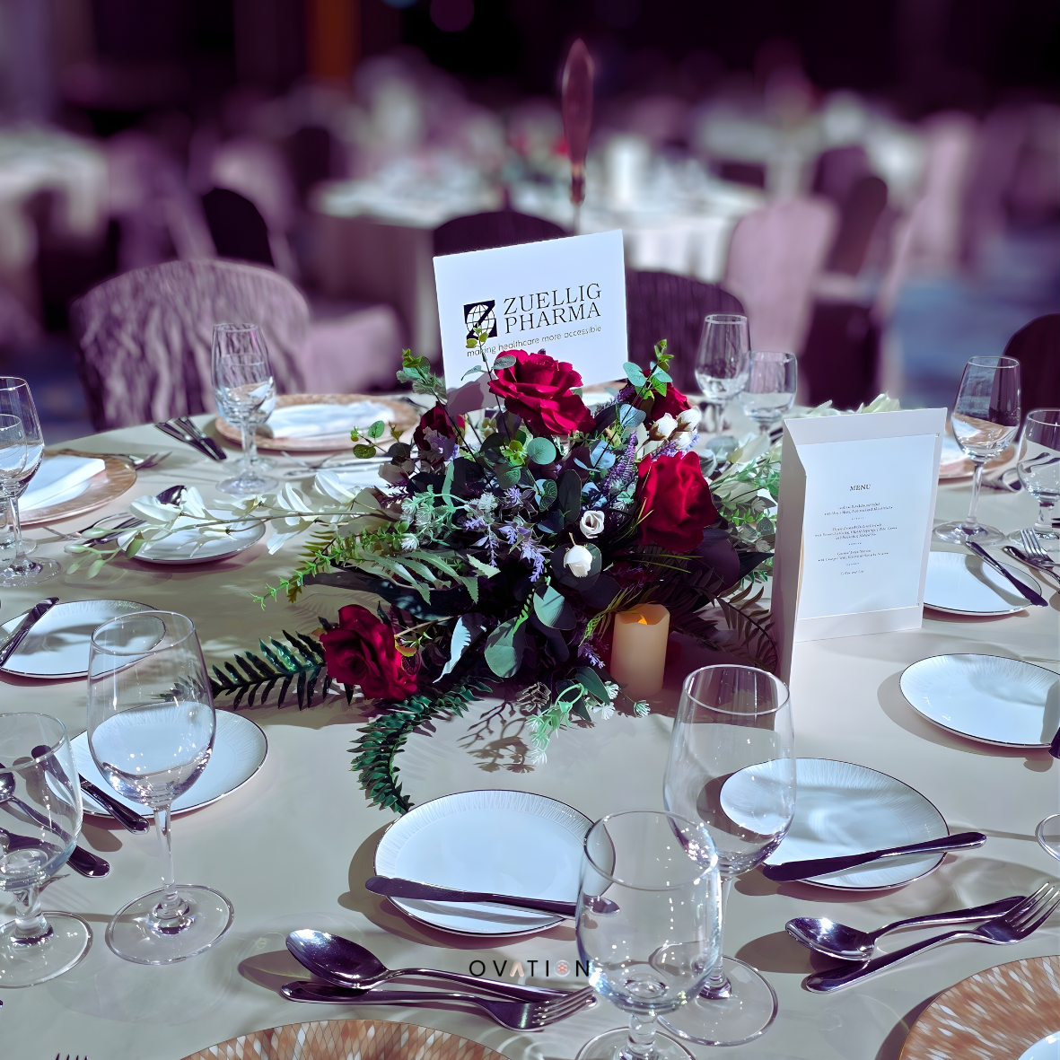 Elegant dining table decorated with a floral centerpiece of red and white roses, greenery, and candles, set with glassware, plates, and silverware for a formal event.