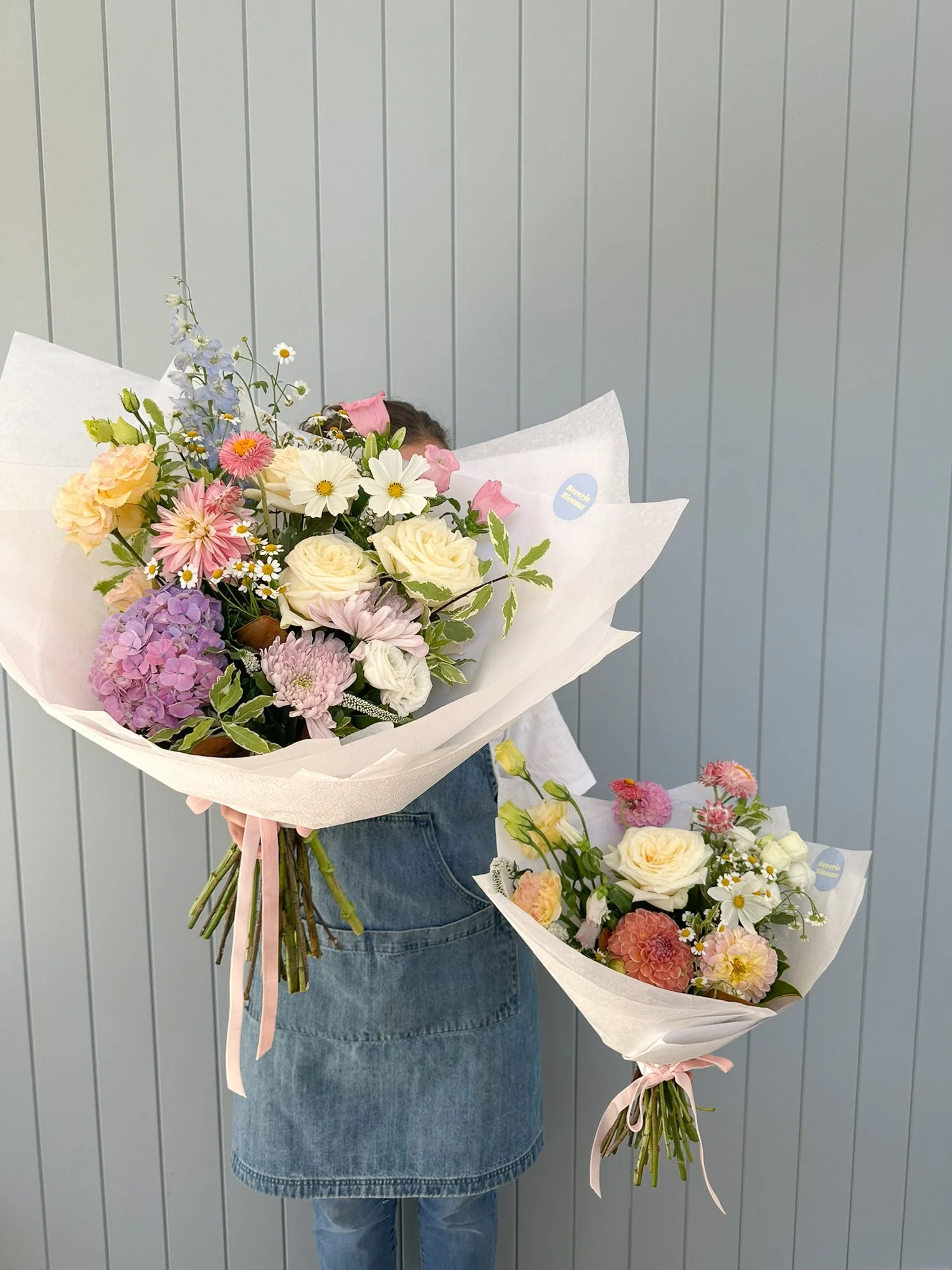 reverie-blooms-florist-holding-two-bouquets-paneled-wall.jpg