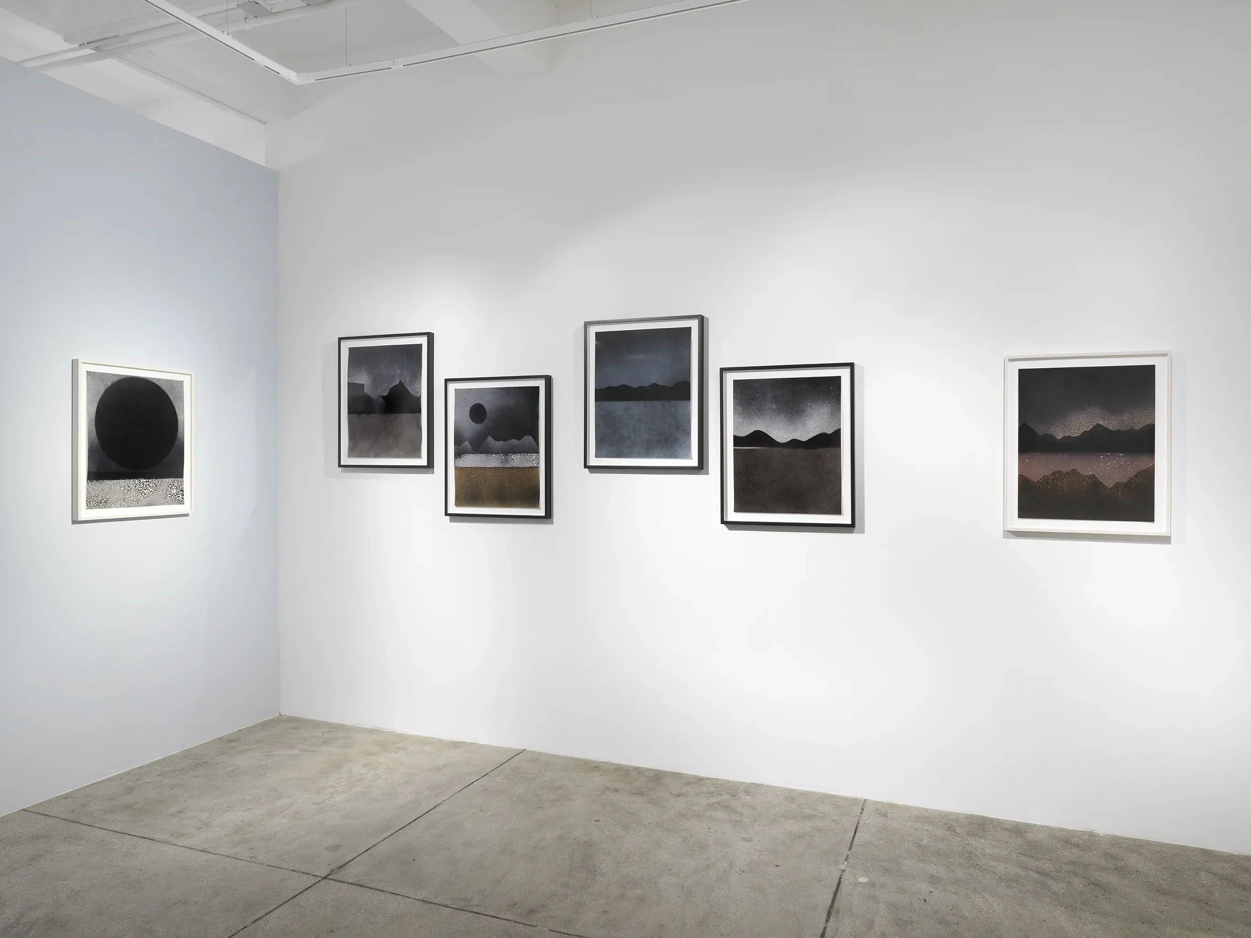 An art gallery with white walls displaying dark landscape paintings in black frames.