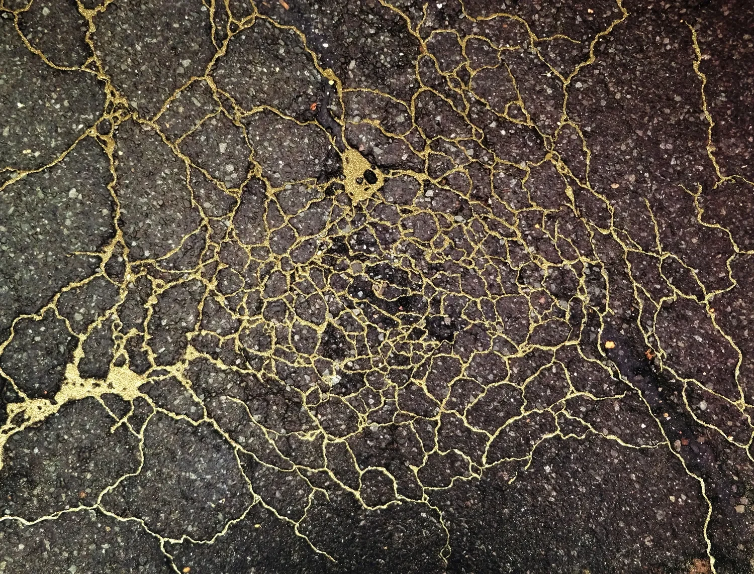 Cracked asphalt pavement with visible yellowish fissures and small debris scattered on the surface.