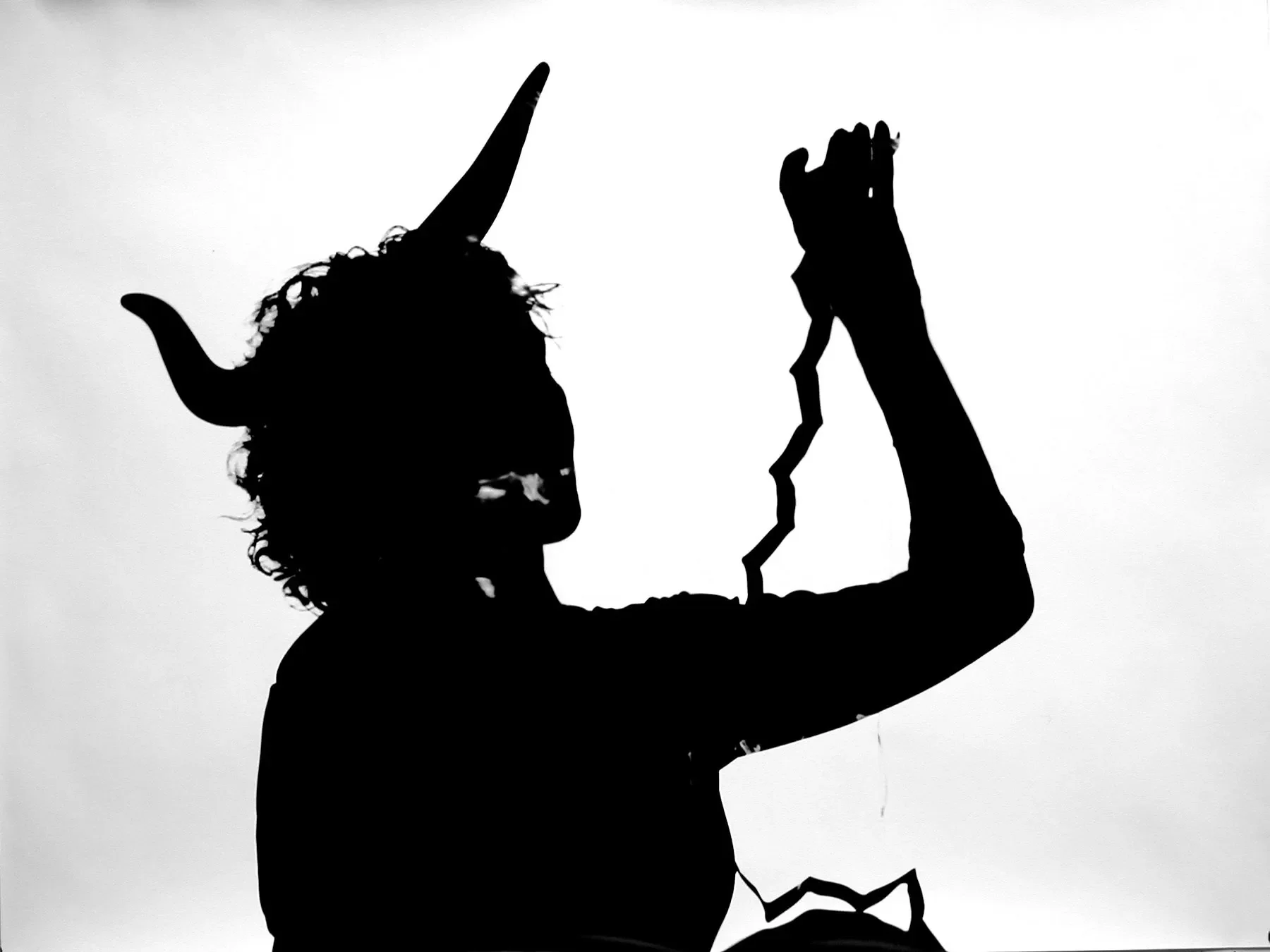 Silhouette of a person with curly hair and horned headgear, holding a small object in their raised hand.