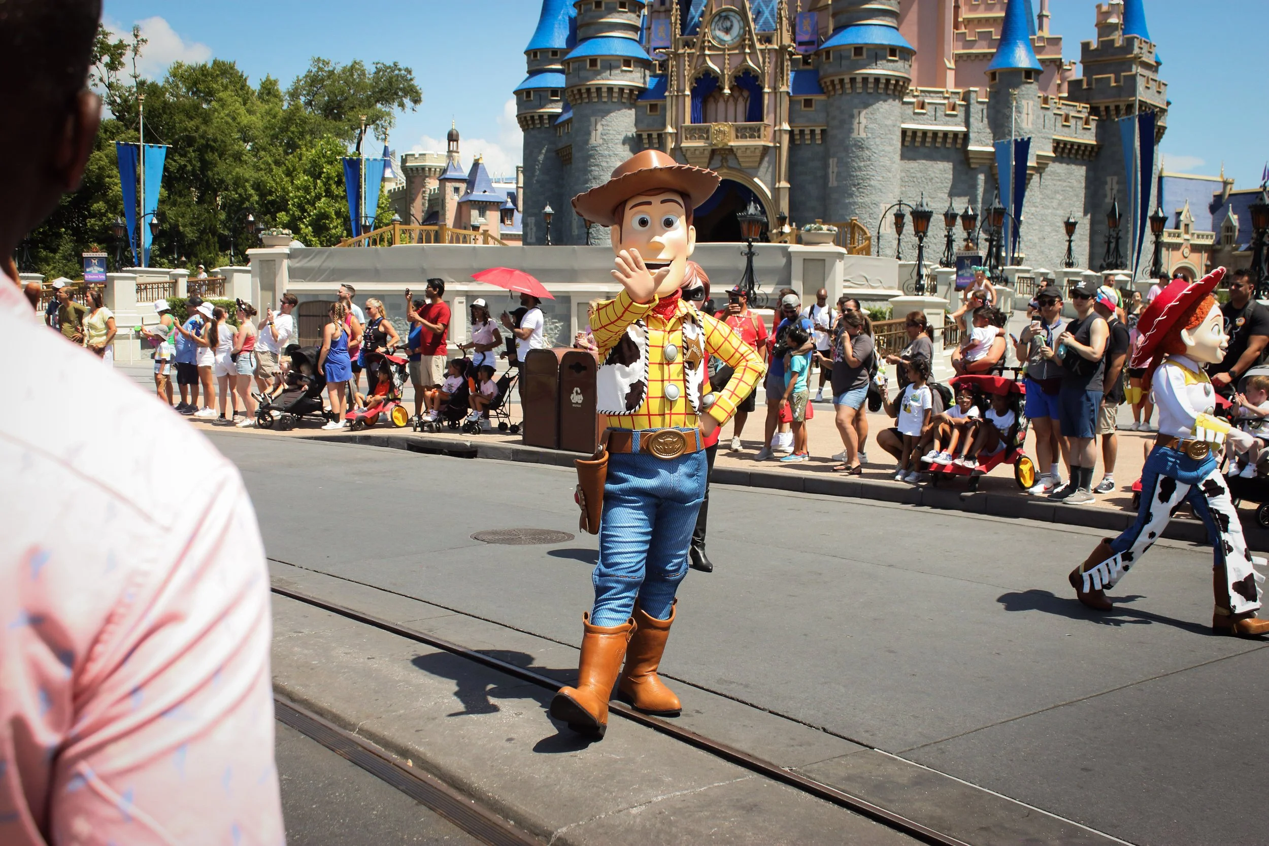 Woody from Toy Story waving to visitors at Disneyland with Sleeping Beauty Castle in the background.