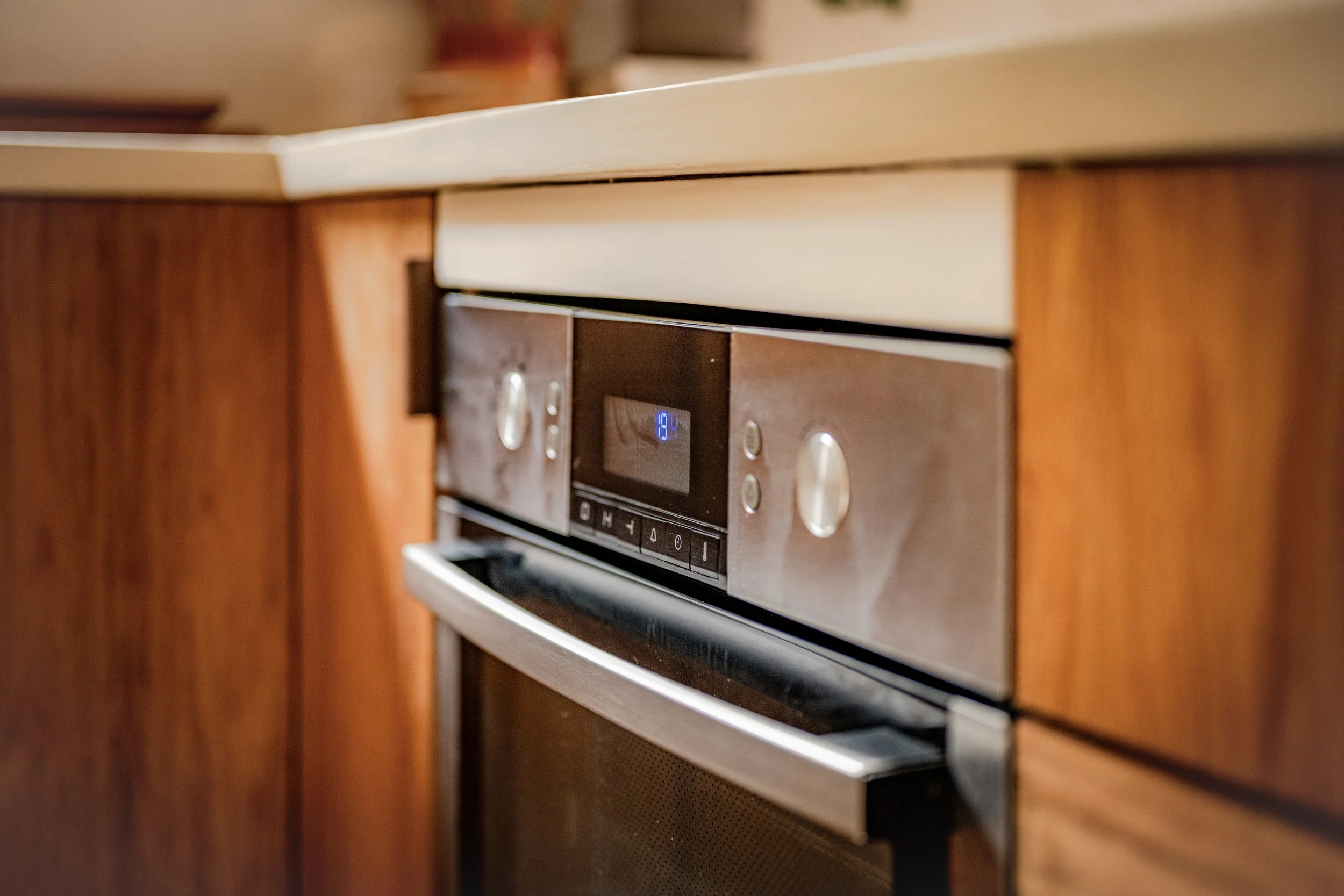Close-up of a modern kitchen oven with digital display, built into wooden cabinetry.