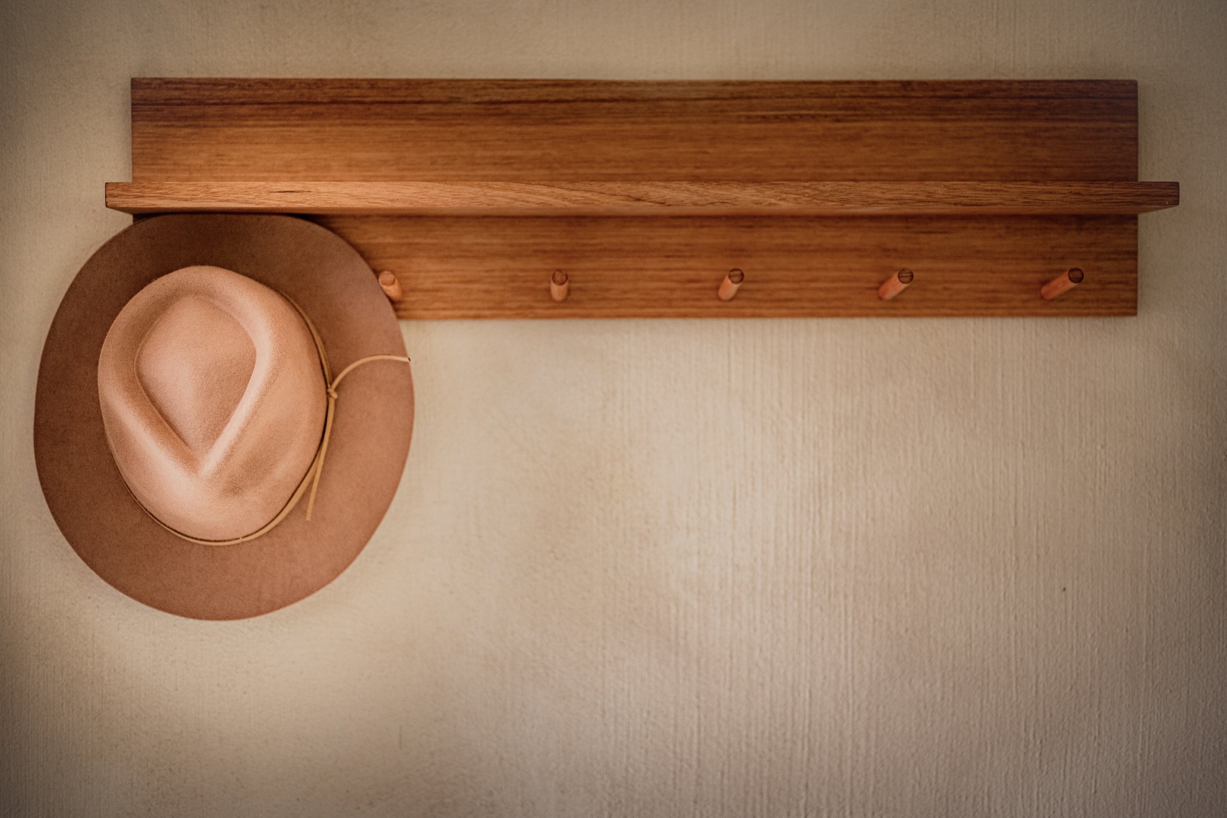 A wooden wall-mounted coat rack with four pegs, with a beige hat hanging on the first peg.