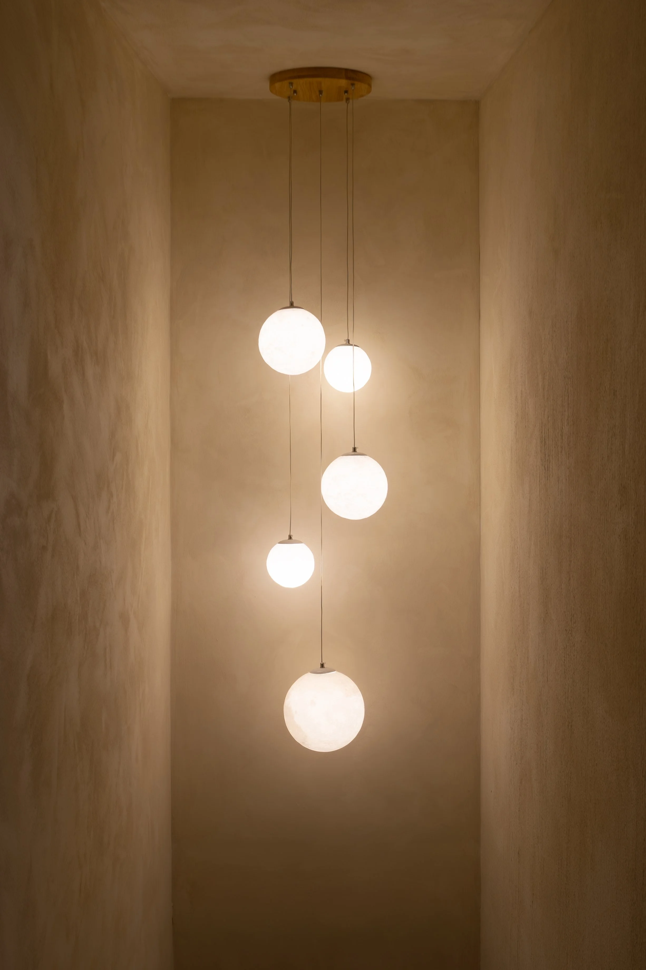 Five spherical pendant lights hanging in a narrow, beige-walled space.