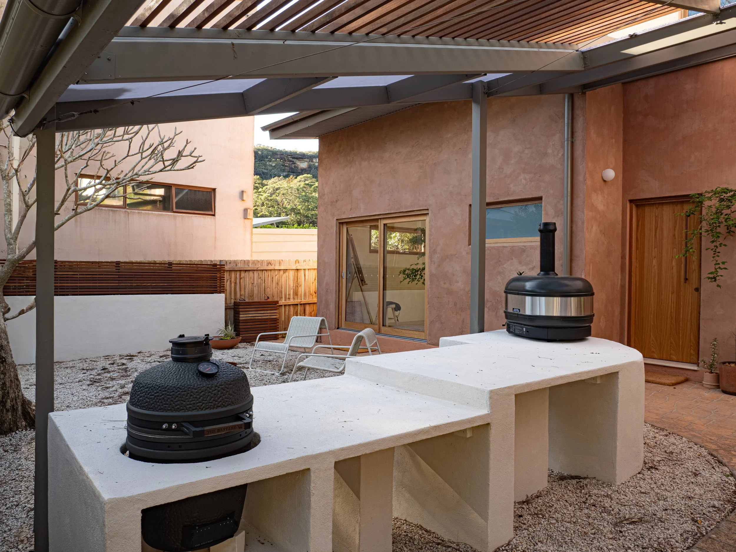 Outdoor kitchen with a Hebel bench, charcoal grill and pizza oven beside the garden wall.