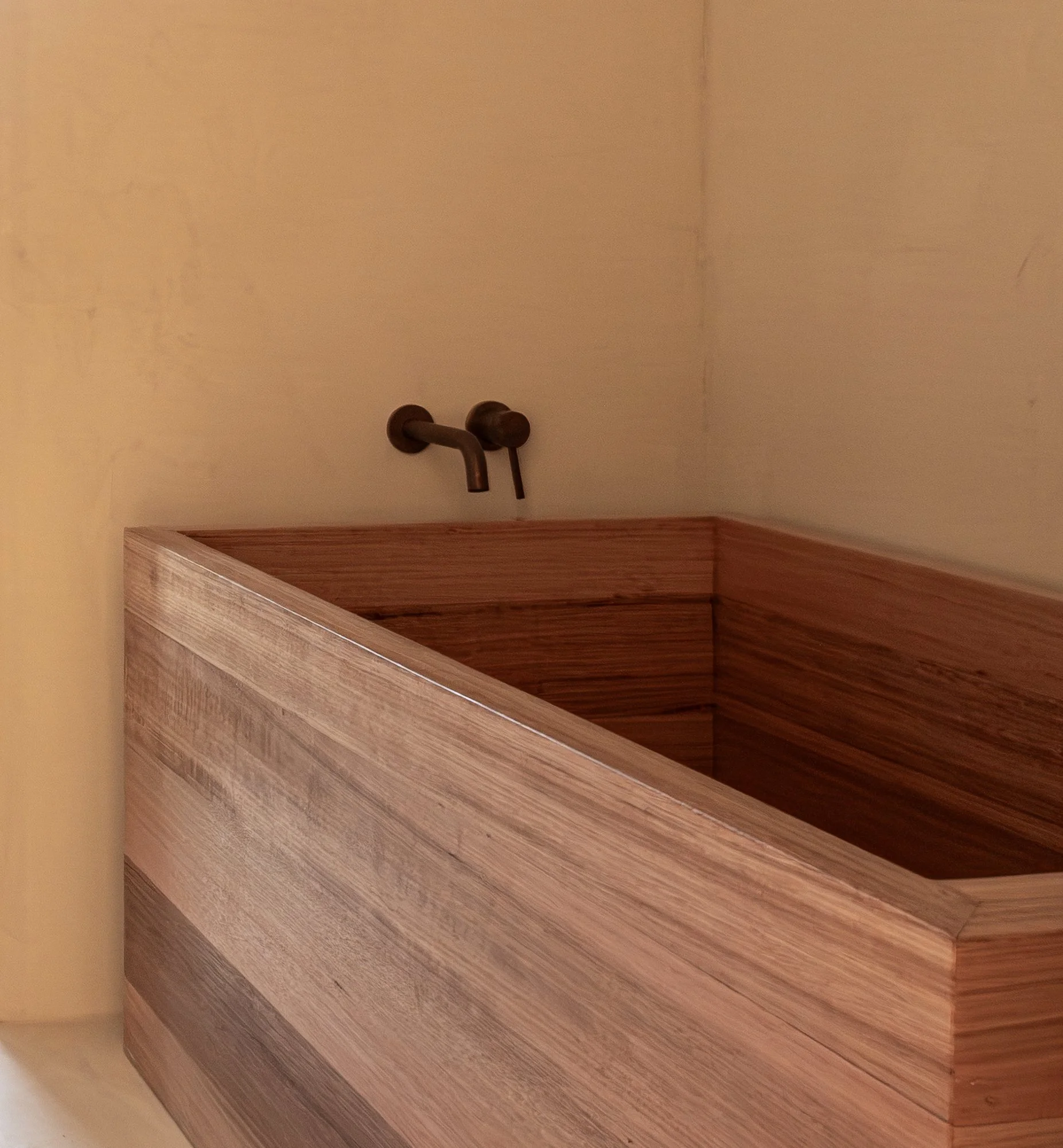Hand-made Victorian Ash soaking bath with bronze tapware against a lime-washed wall.