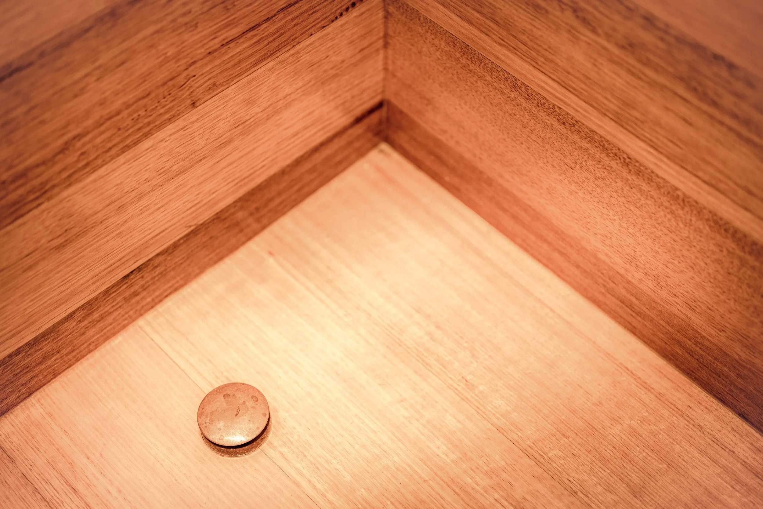 A close-up photo of a wooden drawer interior with a single round metal drawer latch or button at the bottom.