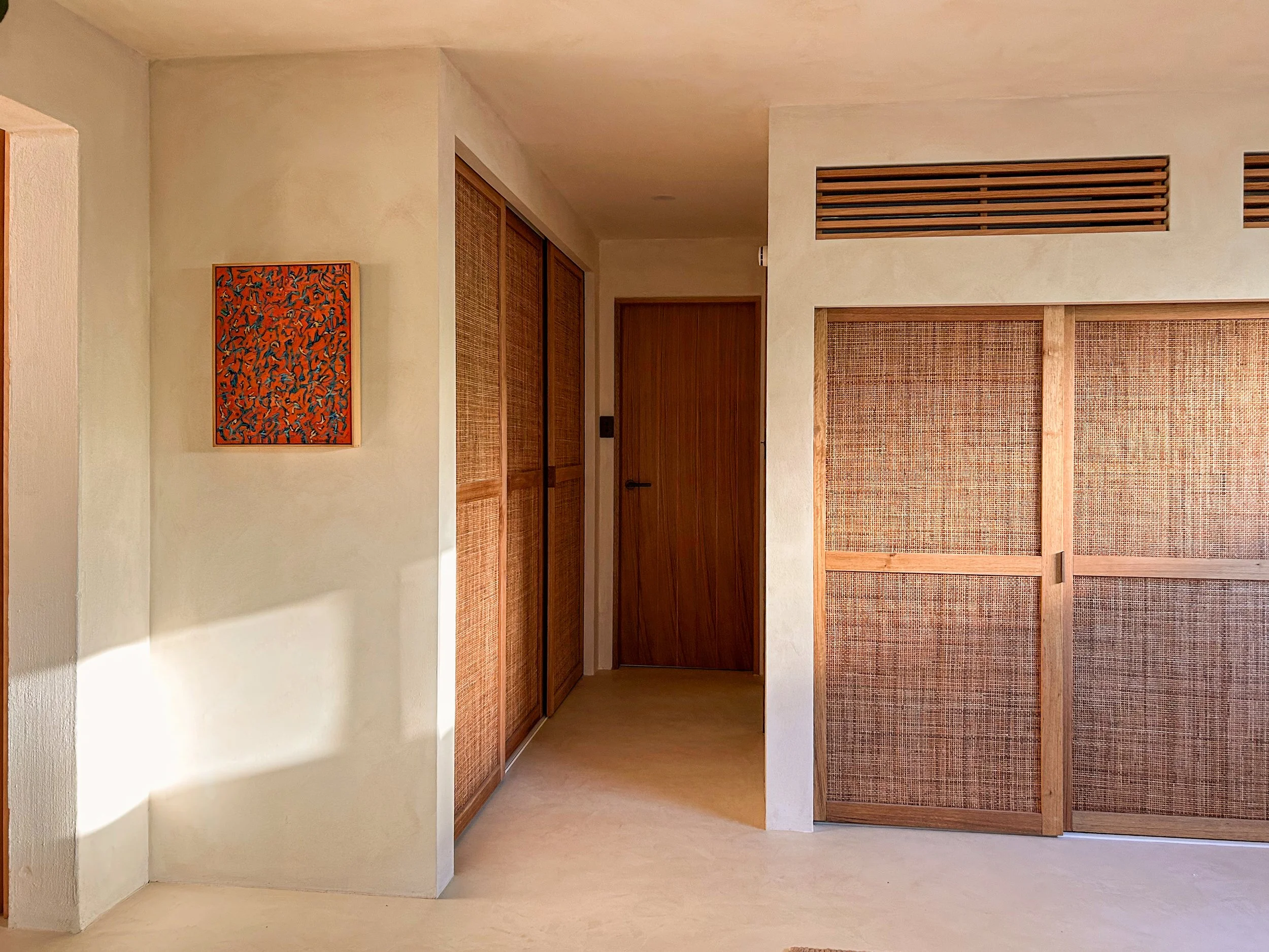Interior view of a room featuring wooden sliding doors with woven rattan panels, wooden accents, and a small abstract painting on the wall.