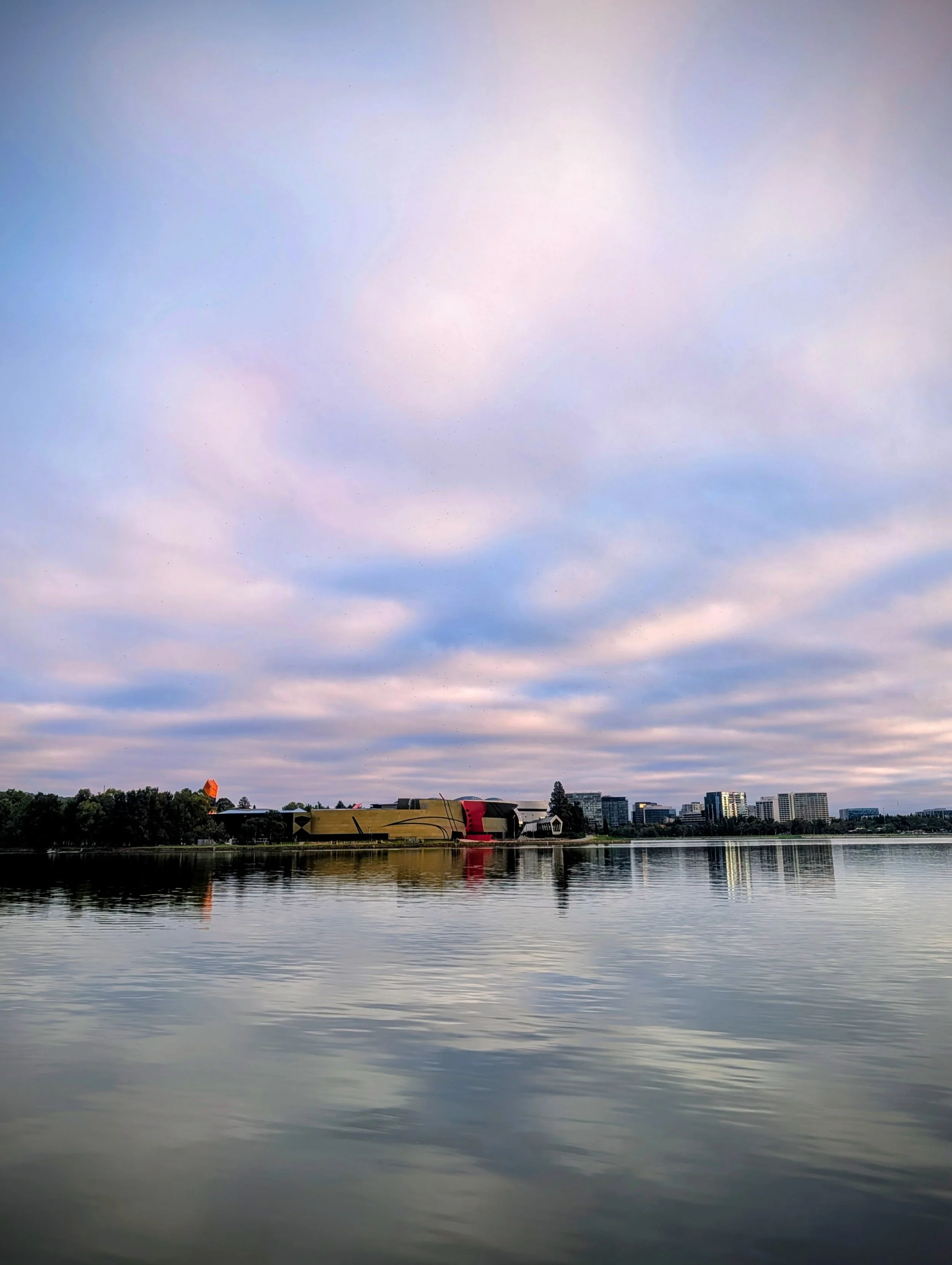 City skyline across a calm body of water under a cloudy sky.