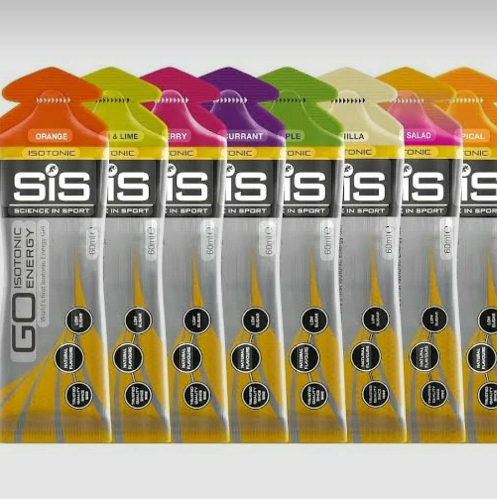 Six bottles of SIS Go Isotonic Energy Drink with different flavors, arranged in a row. The flavors include Orange and Lime, Cherry, Grape, Apple, Vanilla, Salad, and Tropical, as indicated by the colored caps and labels.