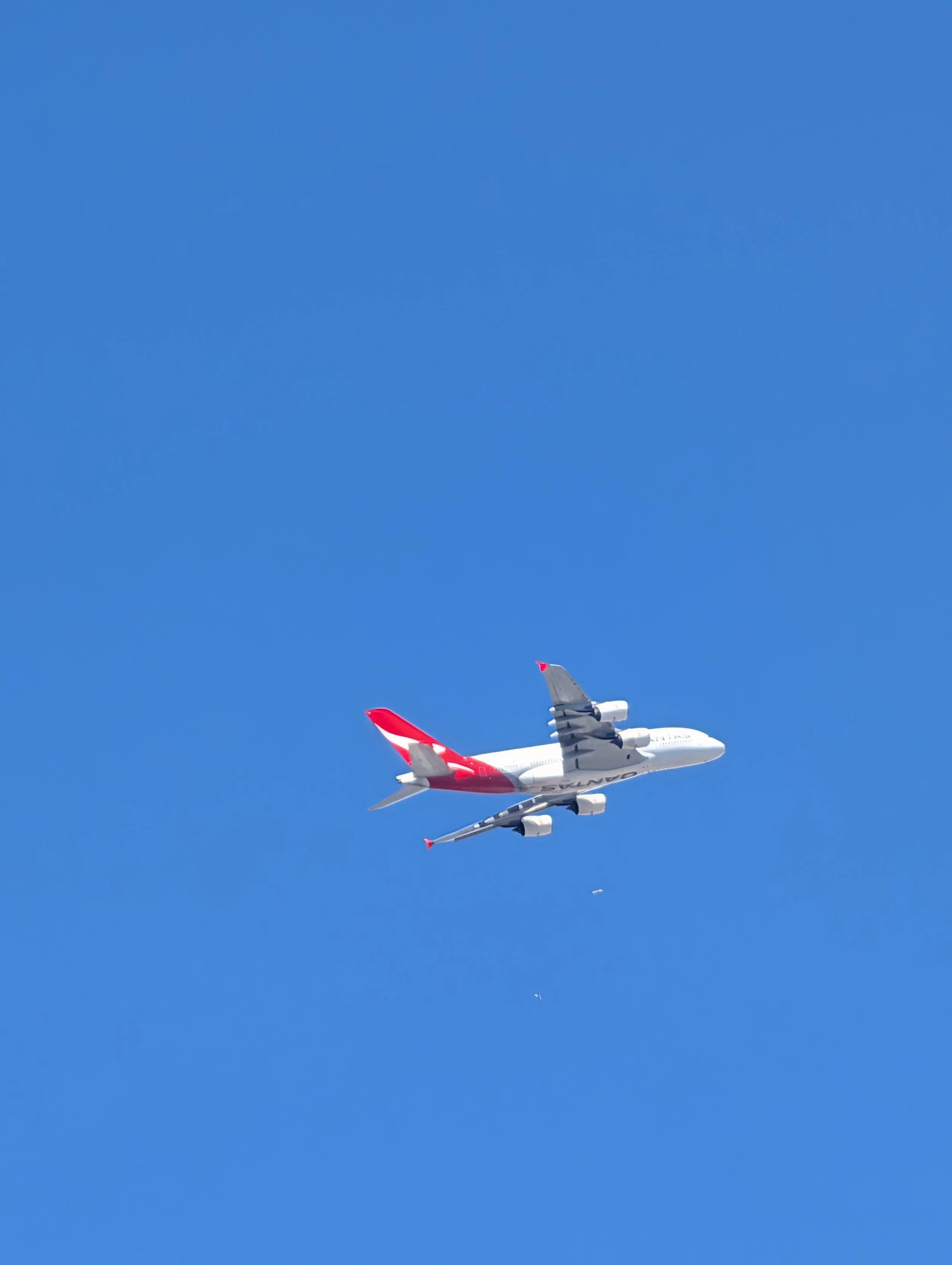A large commercial airplane flying in clear blue sky with a small airplane visible in the distance.