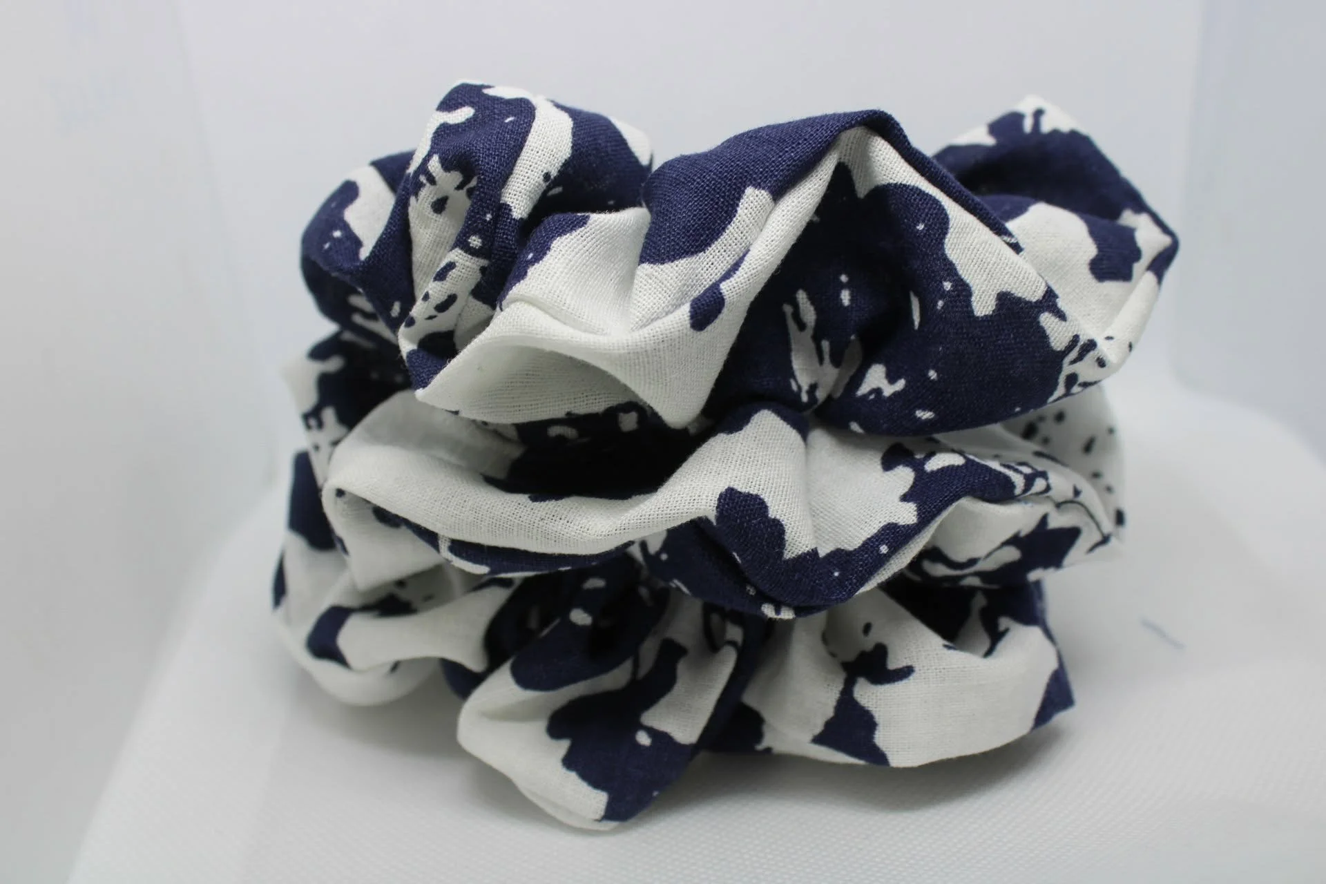 A close-up image of a fabric scrunchie with a blue and white splatter pattern on a white background.