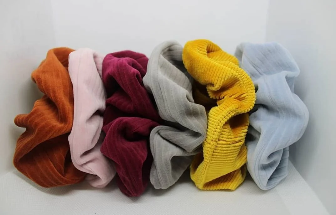 Several crumpled, colorful sock cuffs in shades of orange, pink, red, gray, yellow, and light blue, laid out on a white surface against a white background.