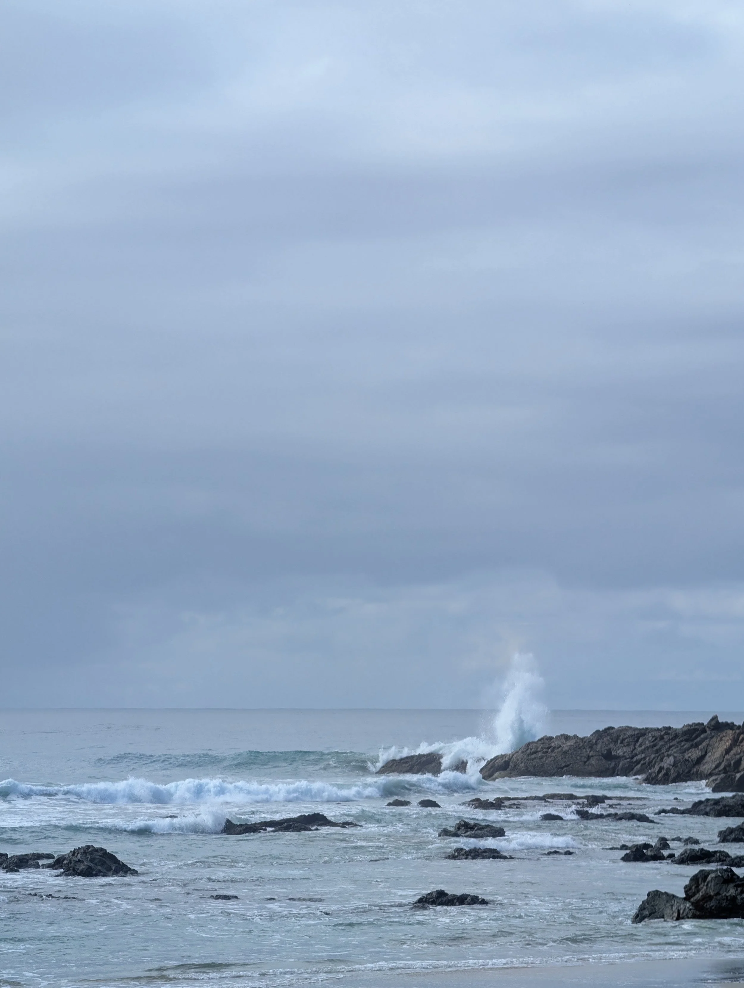Ocean waves crashing against rocks under cloudy sky.