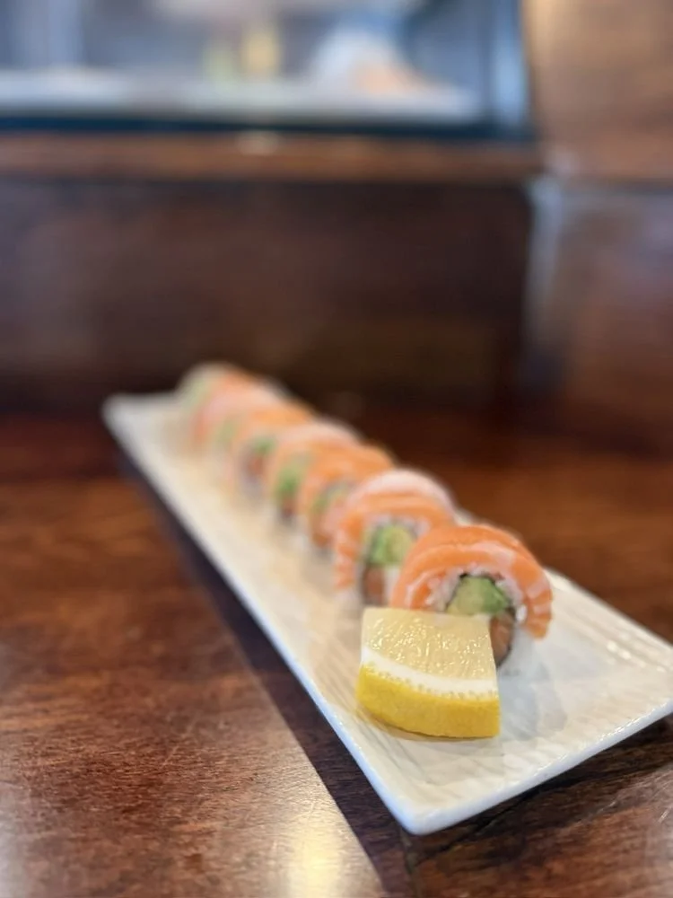 Sushi rolls with sliced lemon on a rectangular white plate on a wooden table.