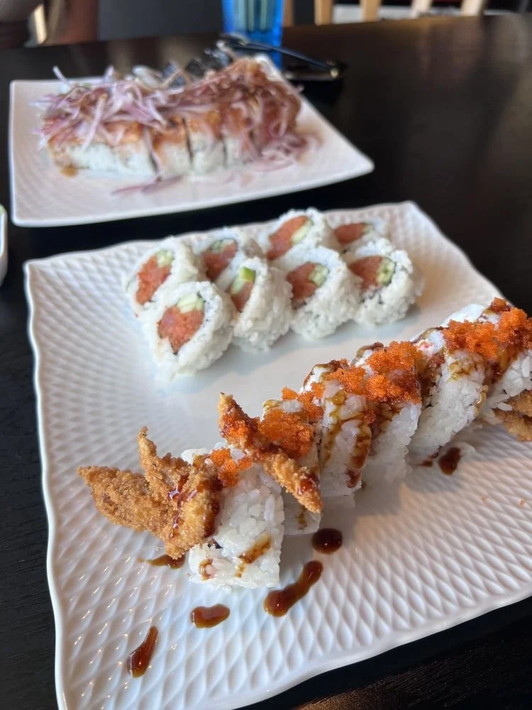 Three plates of sushi on a dark table, featuring rolls with various toppings and sauces.