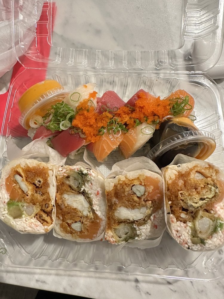 A plastic container of assorted sushi with sliced rolls and sashimi garnished with fish roe and green onions.
