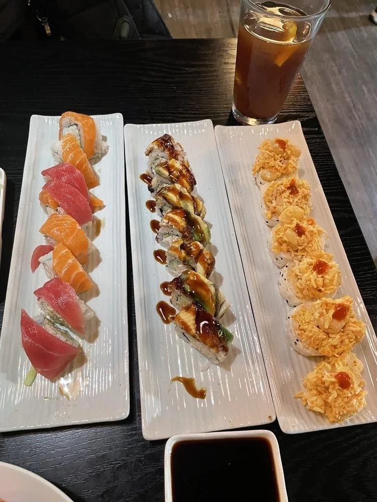 Three plates of sushi rolls, a glass of iced tea, and a small bowl of soy sauce on a dark wooden table.