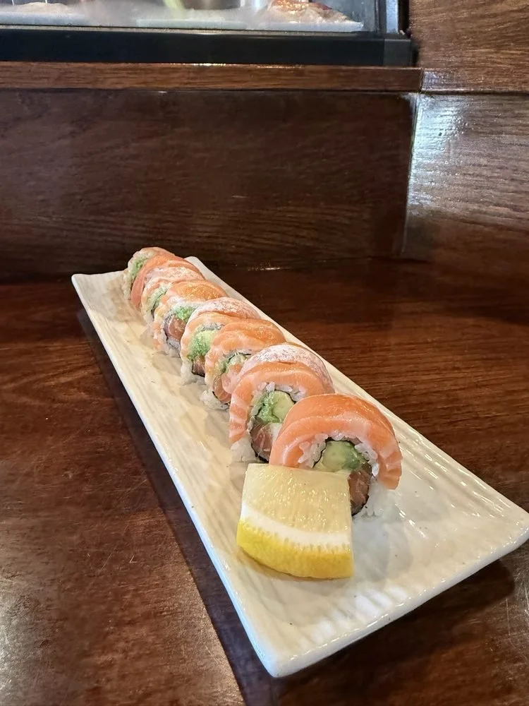 Sushi roll platter with slices of salmon, avocado, and rice, garnished with a lemon wedge on a rectangular plate.